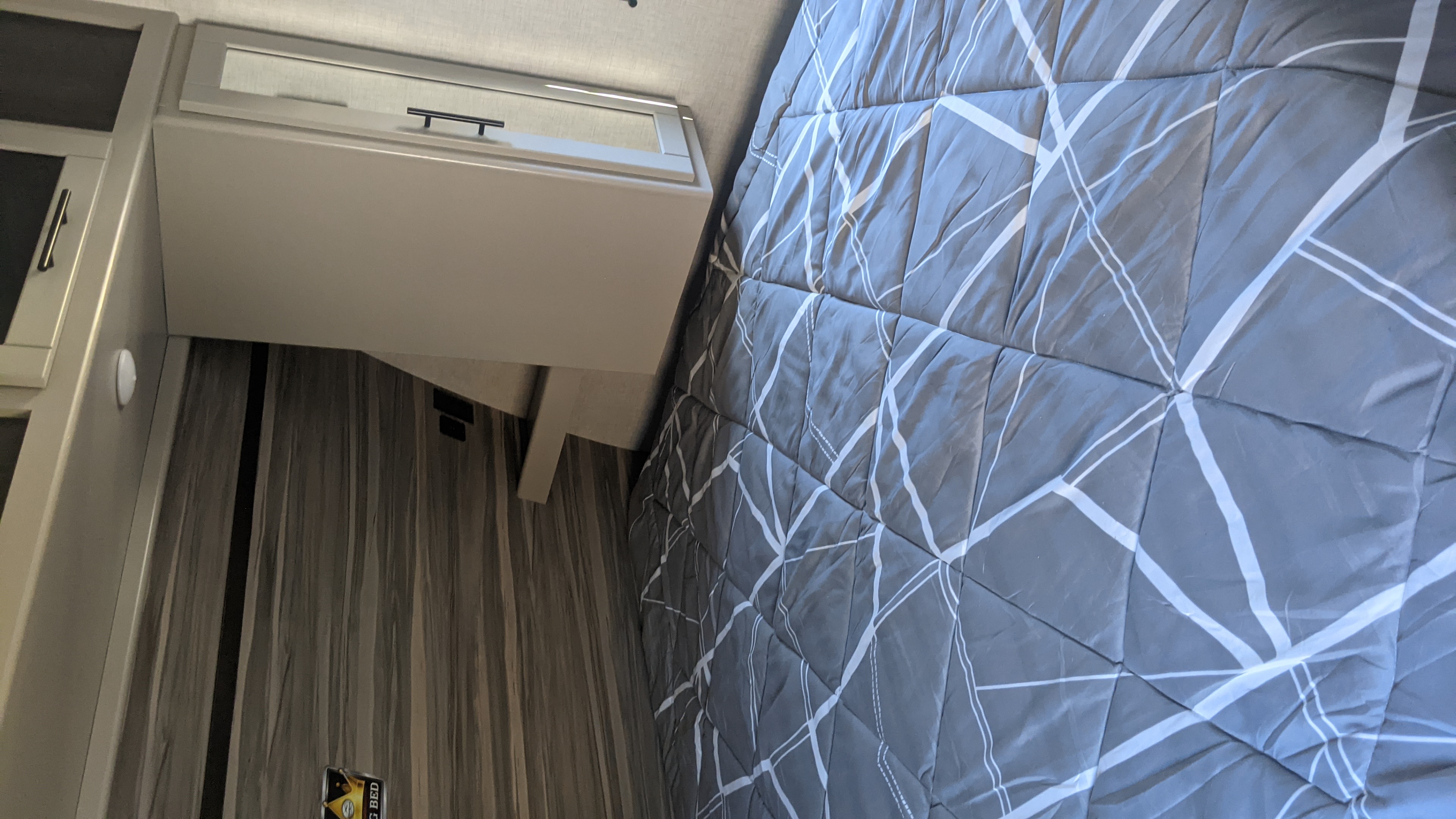 Modern RV rental bedroom featuring a grey bed with a geometric comforter and built-in overhead cabinets.. Crossroads Cruiser Aire 2022