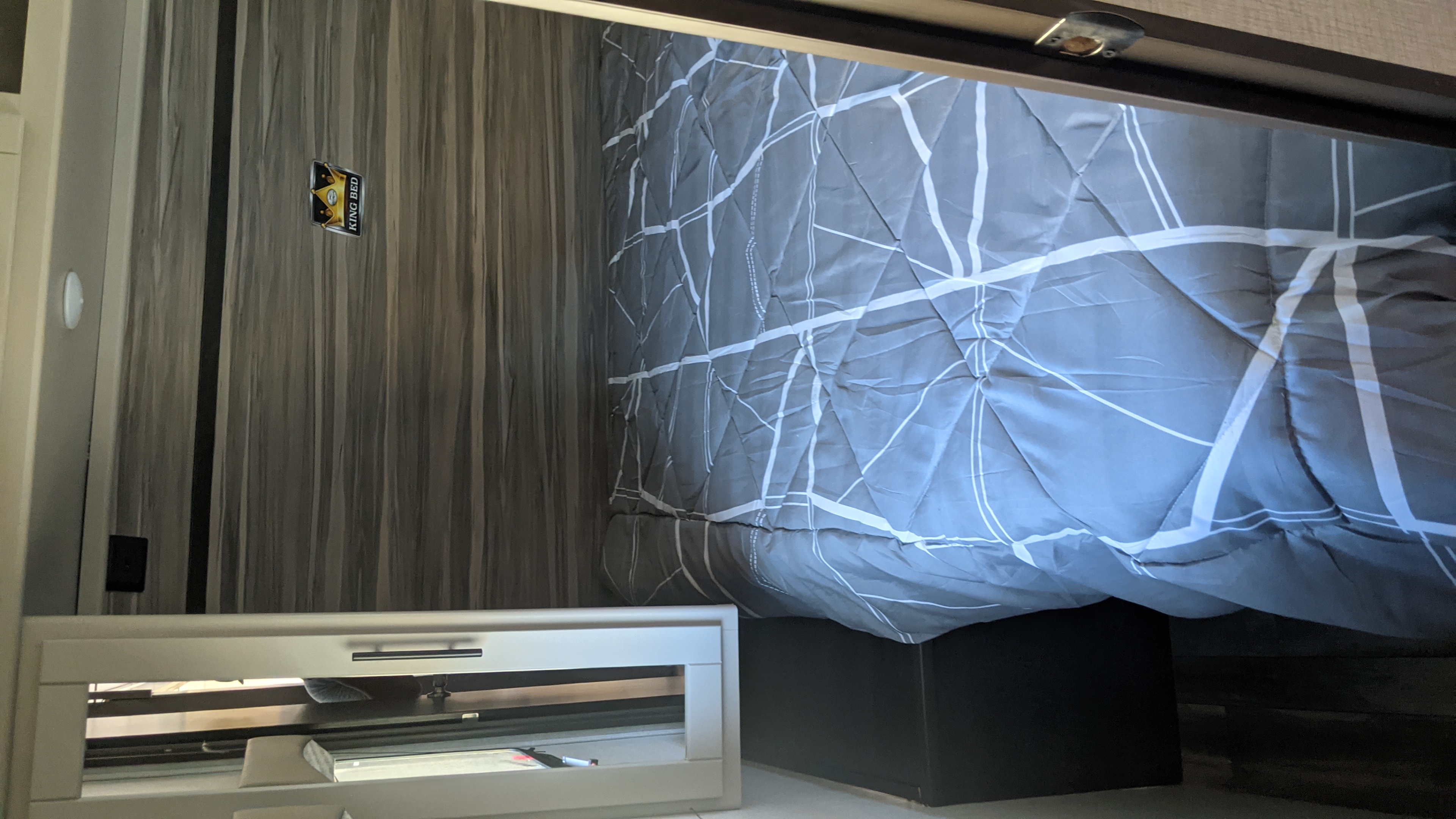 RV rental king bed in a modern bedroom, with a grey comforter and wood-grain walls. Ideal for comfortable travel.. Crossroads Cruiser Aire 2022