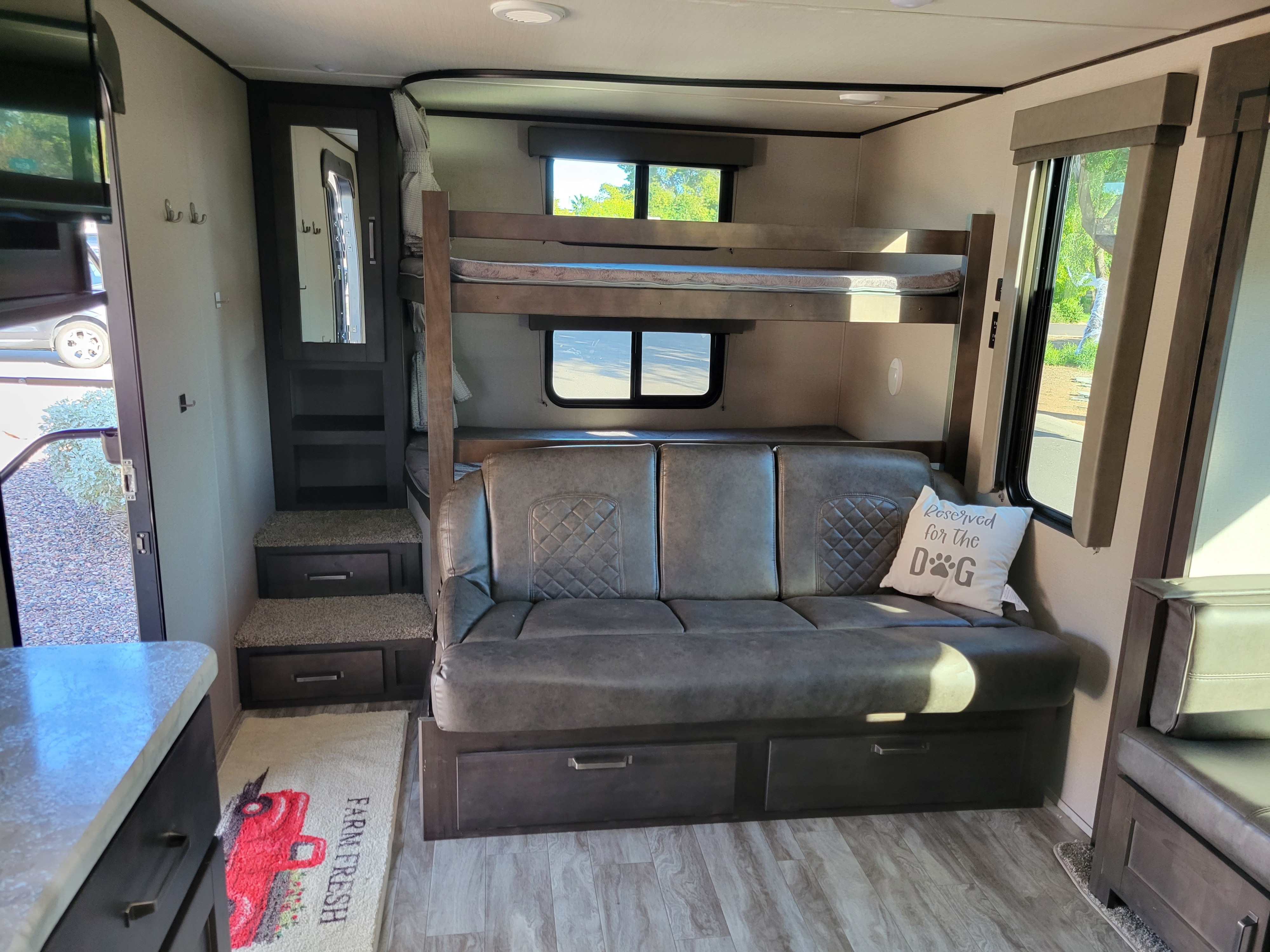 Bright RV rental interior: bunk beds, a gray sofa bed with storage, and windows showing outdoor greenery.. Grand Design 265bh 2021
