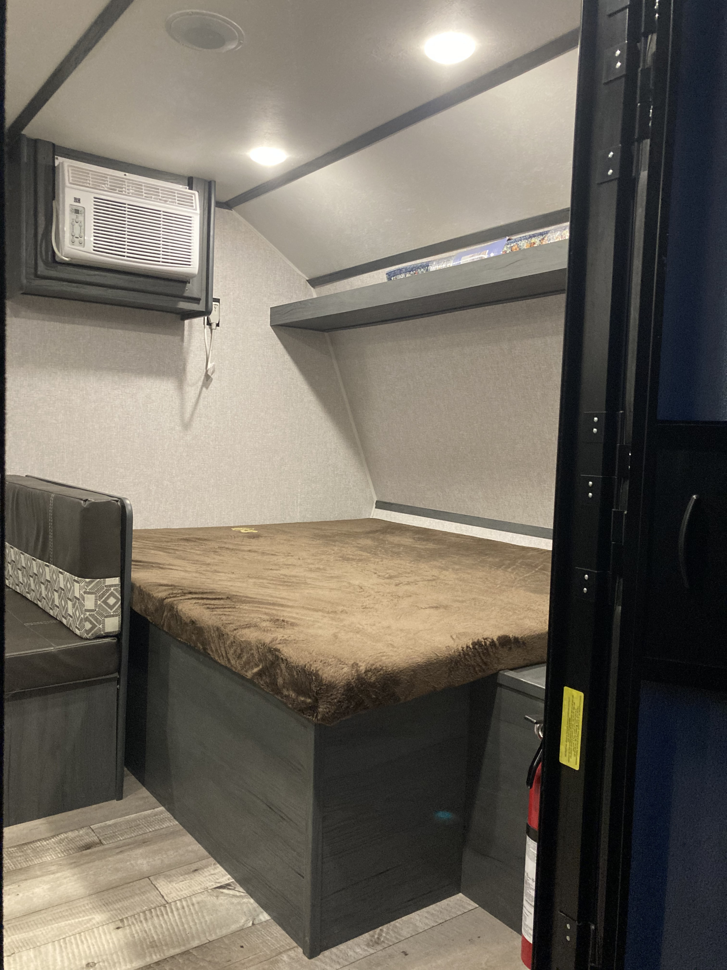 Compact RV rental interior featuring a cozy bed, dinette seating, AC unit, and overhead shelf.. Dutchmen Aspen Trail 2021