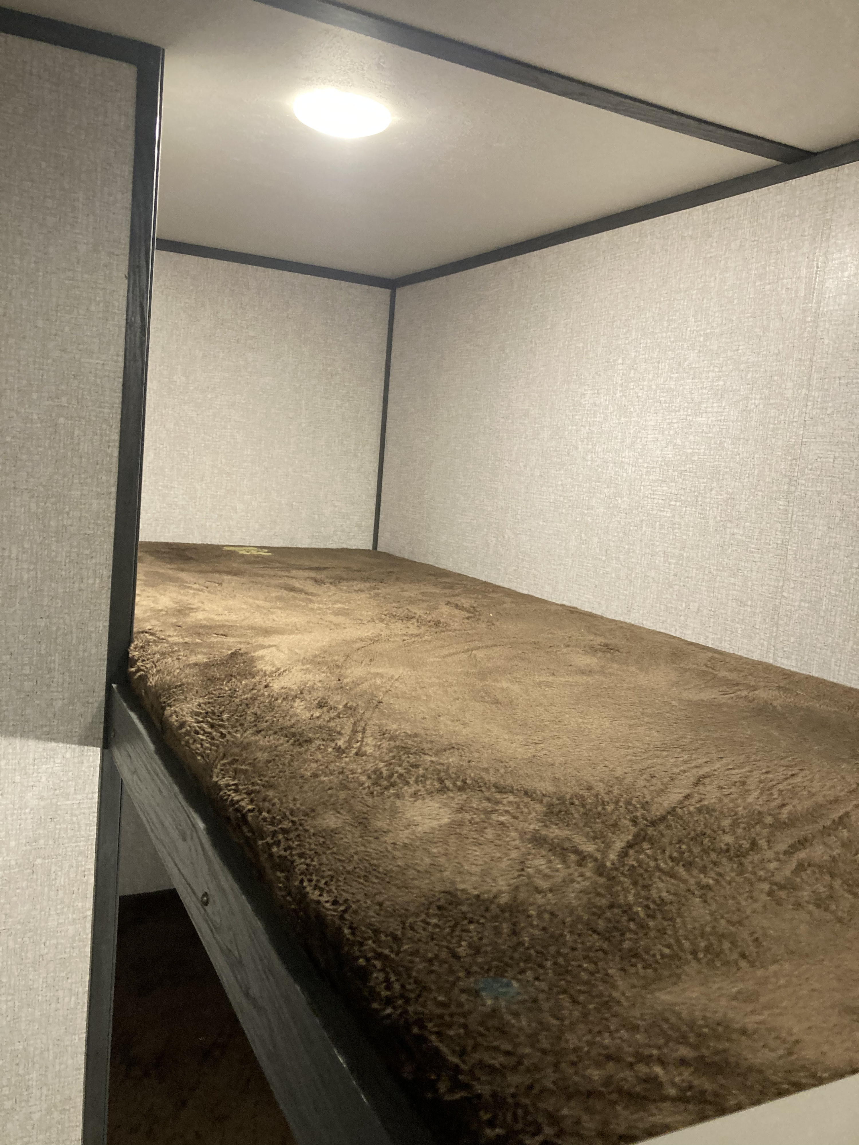RV rental interior features a cozy bunk bed with a soft brown mattress and an overhead light, ideal for compact sleeping.. Dutchmen Aspen Trail 2021