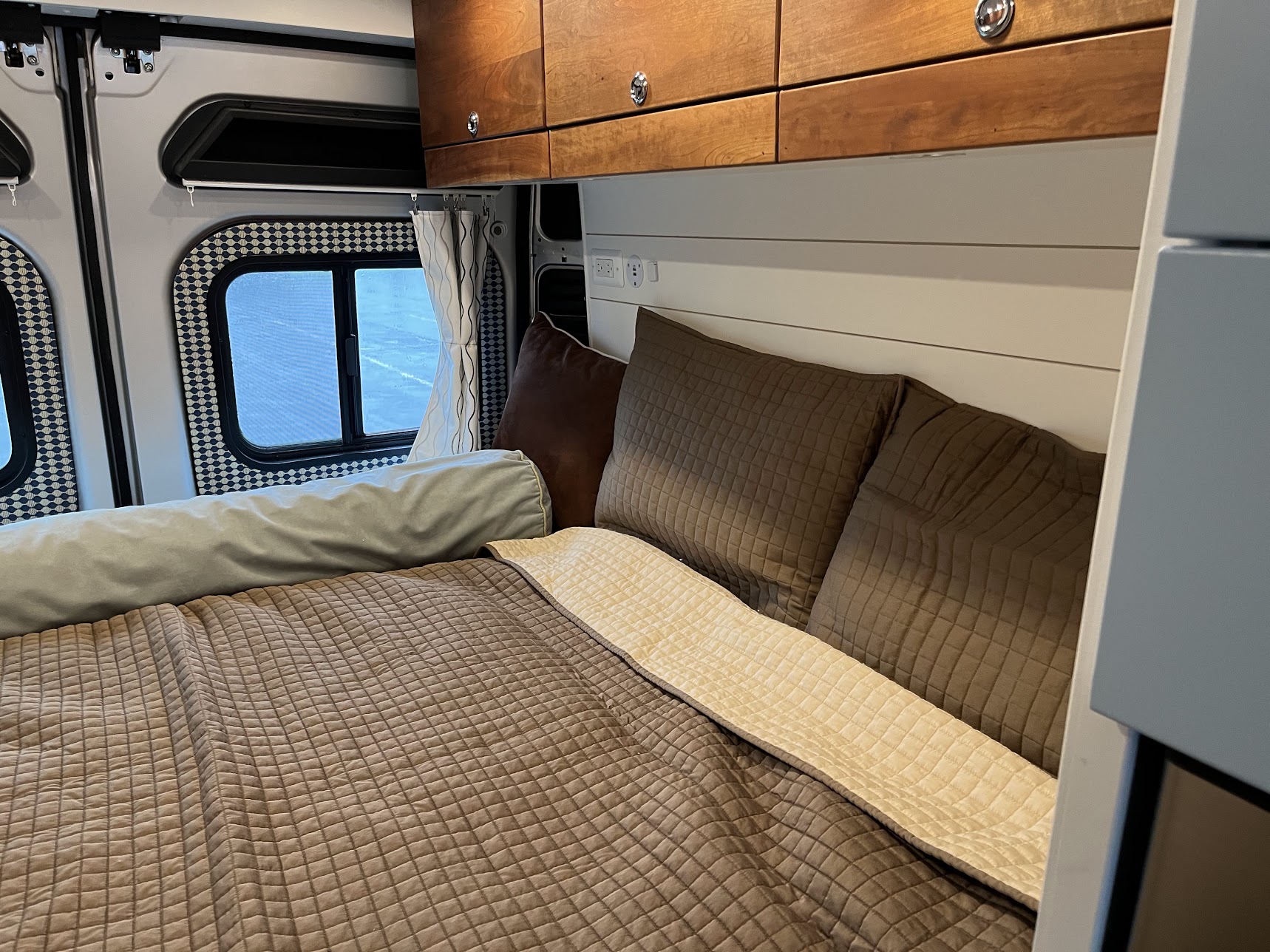 Cozy RV rental bedroom with brown quilted bedding, bolster, wooden cabinets, and white shiplap wall.. Ram Promaster 2500 2020