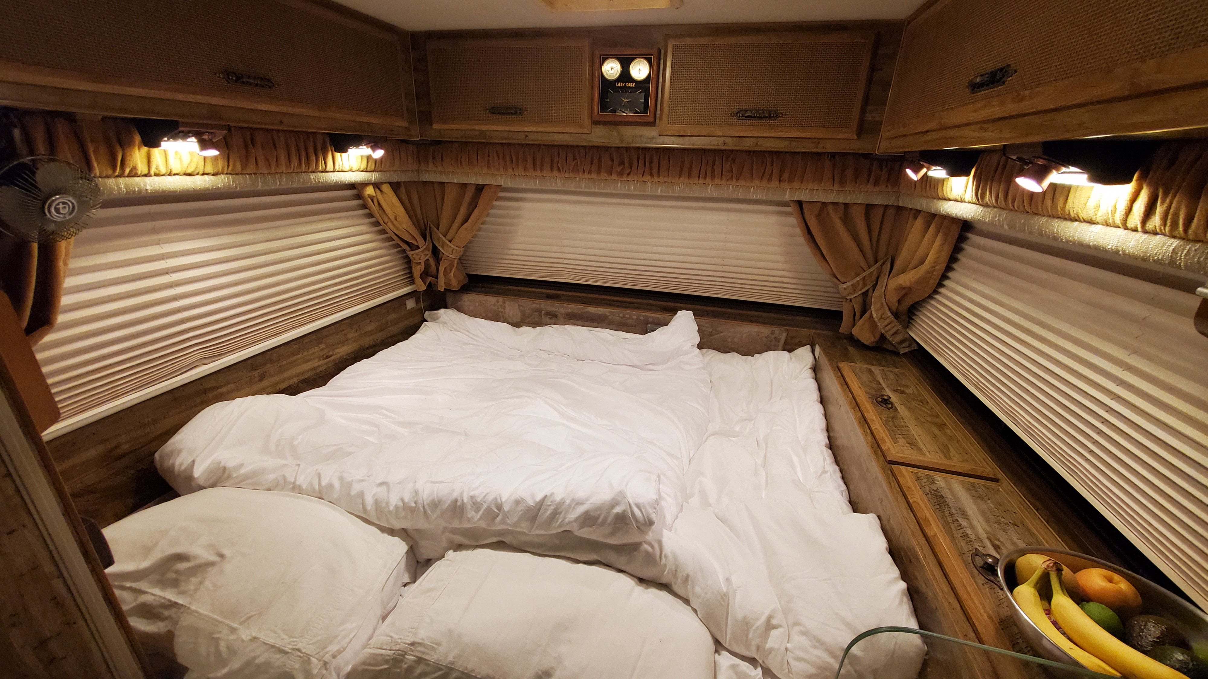 RV rental bedroom: white bed, wood cabinets, pleated blinds, and warm lighting create a cozy space.. Lazy Daze 22 1987