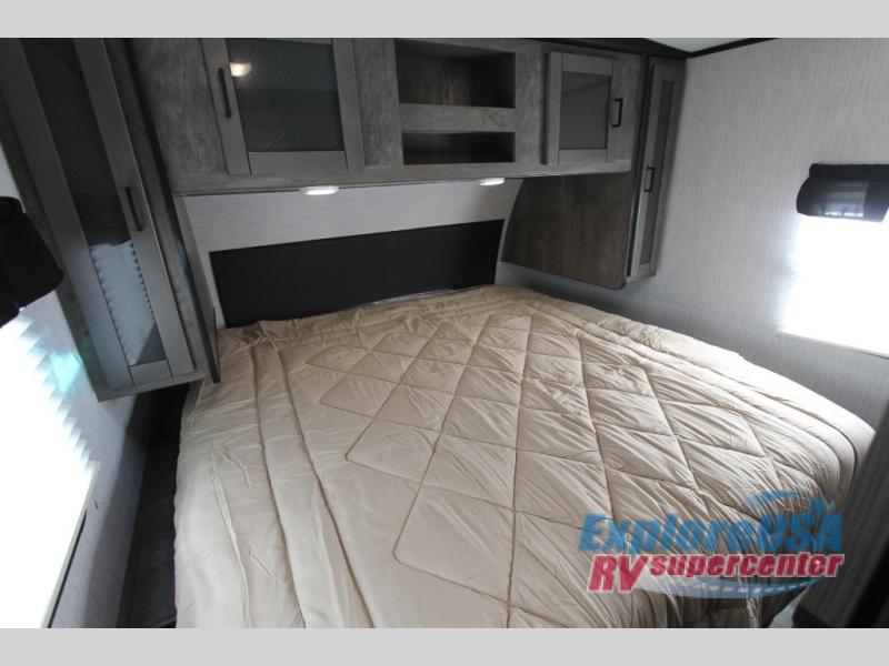 Cozy RV rental bedroom interior features a made bed with light comforter, headboard, and overhead storage cabinets.. Heartland North Trail 2021