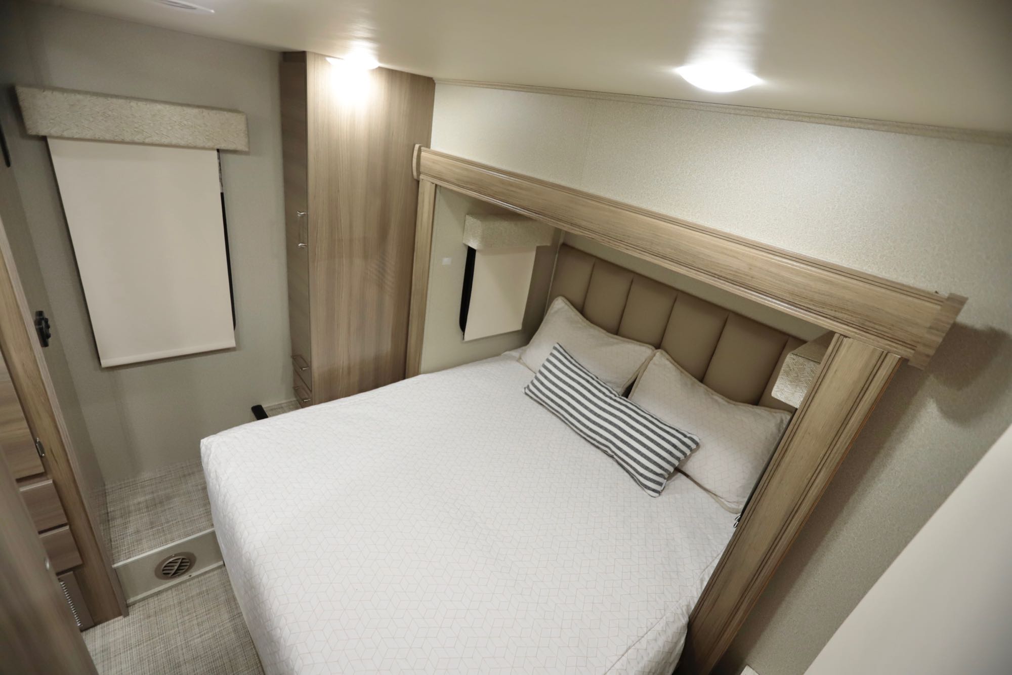 Cozy RV rental bedroom featuring a comfortable bed with neutral decor, built-in storage, and a window with shade.. Jayco Qwest 2019