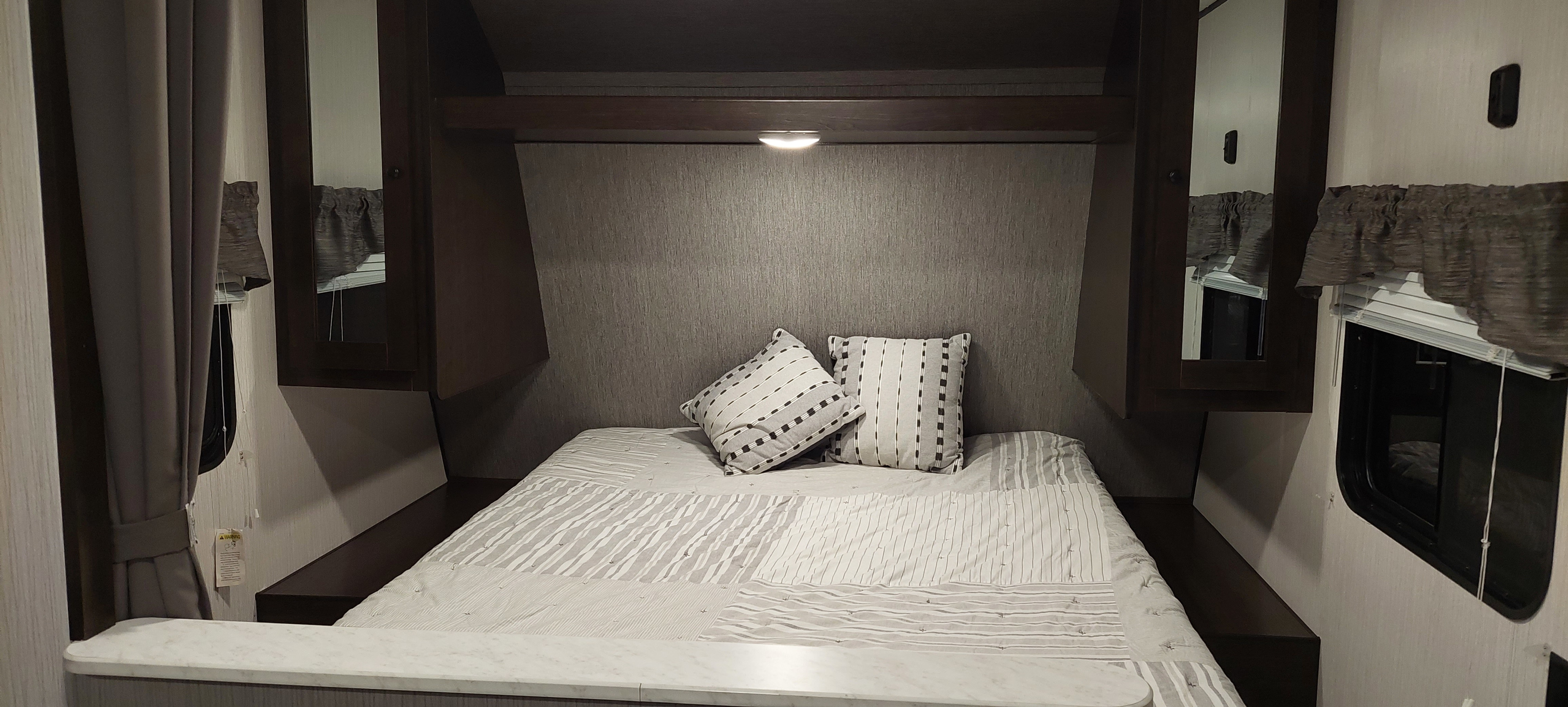 Cozy RV rental bedroom featuring a comfortable bed with patterned pillows, overhead storage, and windows.. Heartland Prowler 2019