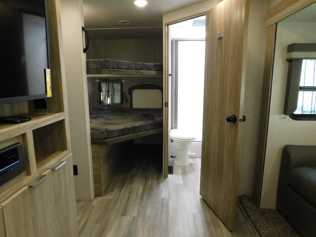 This RV rental interior features a bunk bed area, a built-in entertainment unit with TV, and an open door to a compact bathroom.. Winnebago Minnie 2021