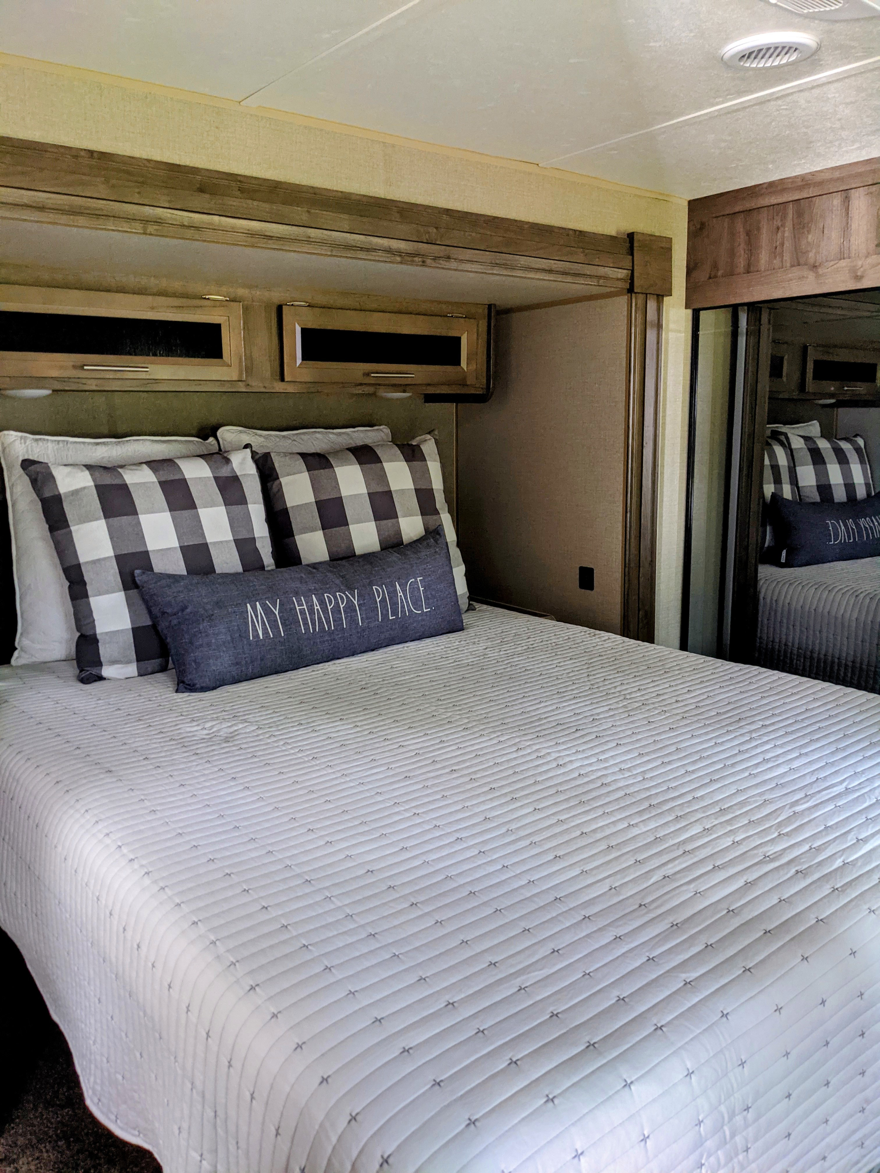 Cozy RV rental bedroom with a white quilted bedspread, buffalo check pillows, and an "MY HAPPY PLACE" cushion.. Forest River euroa 2021