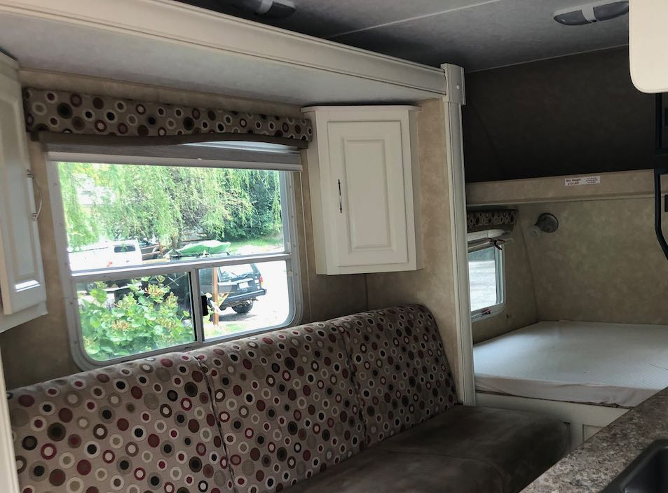 RV rental interior featuring a patterned sofa, a window with outdoor view, and a cozy bed area.. Cruiser RV Shadow Cruiser 2010