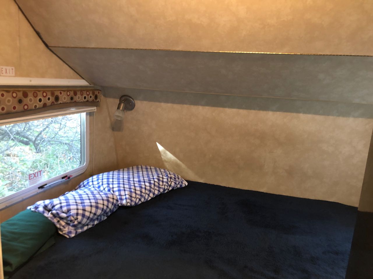 An inviting RV rental bed area with a dark blue blanket, plaid pillows, and a bright window. Your cozy mobile escape!. Cruiser RV Shadow Cruiser 2010