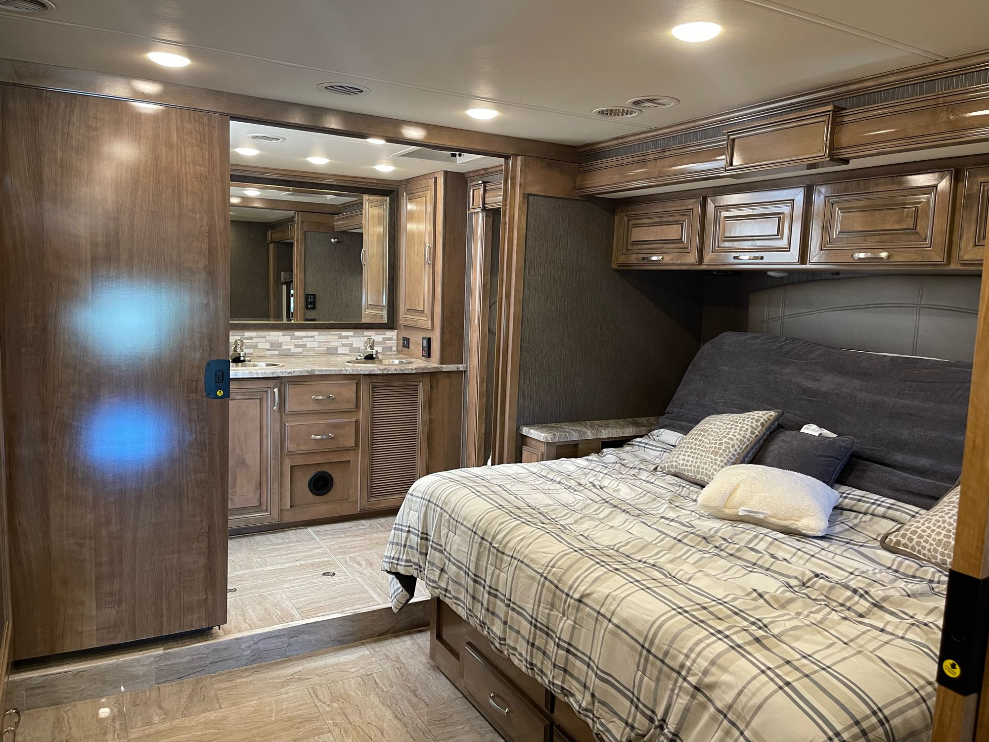 RV rental interior: a bedroom with a large bed on the right, and a spacious bathroom with dual vanity on the left.. Thor Motor Coach Aurora 2020