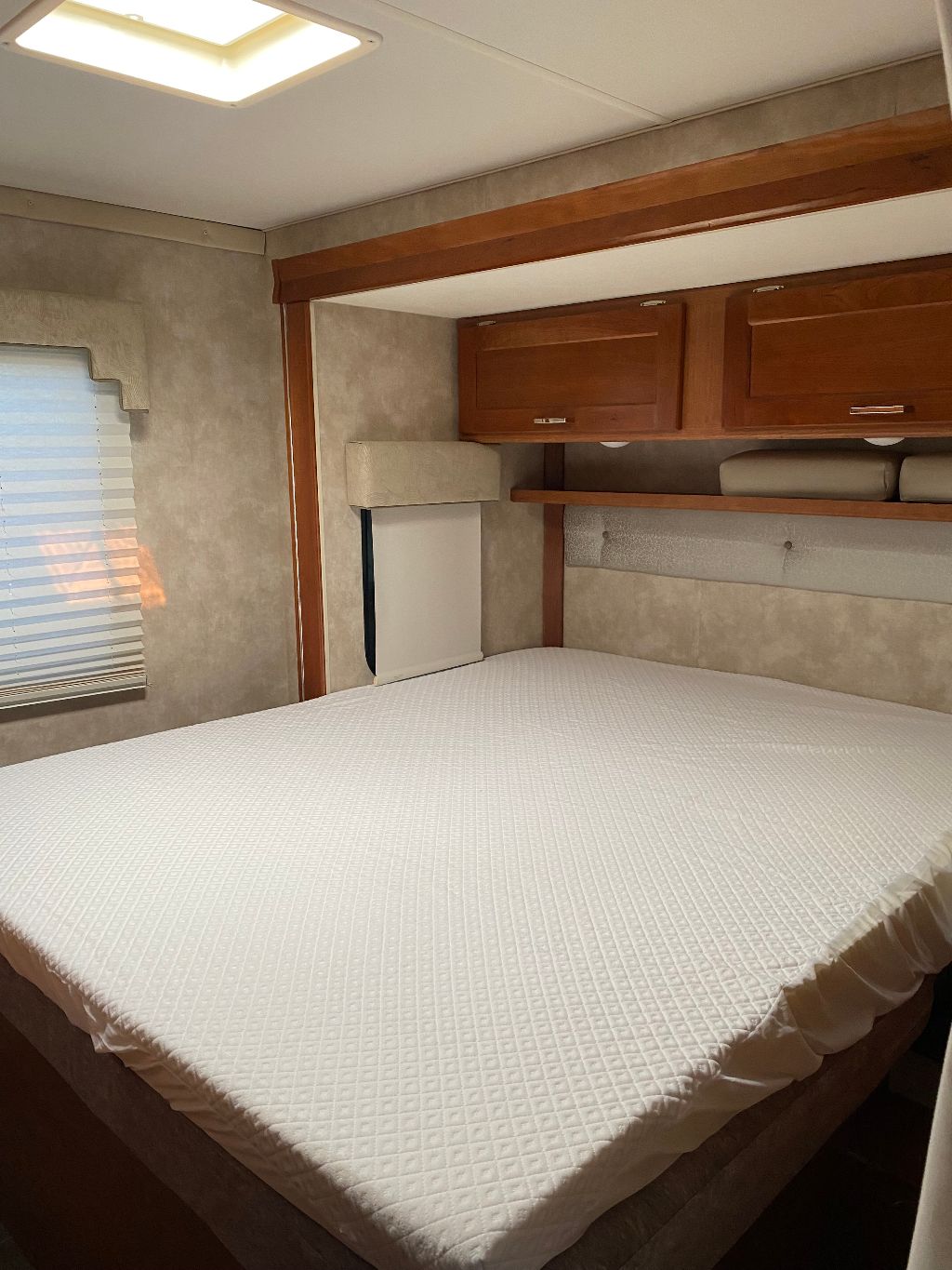 Comfortable RV rental bedroom with a large bed, overhead wood cabinets, window, and skylight.. Winnebago Minnie Winnie 2019