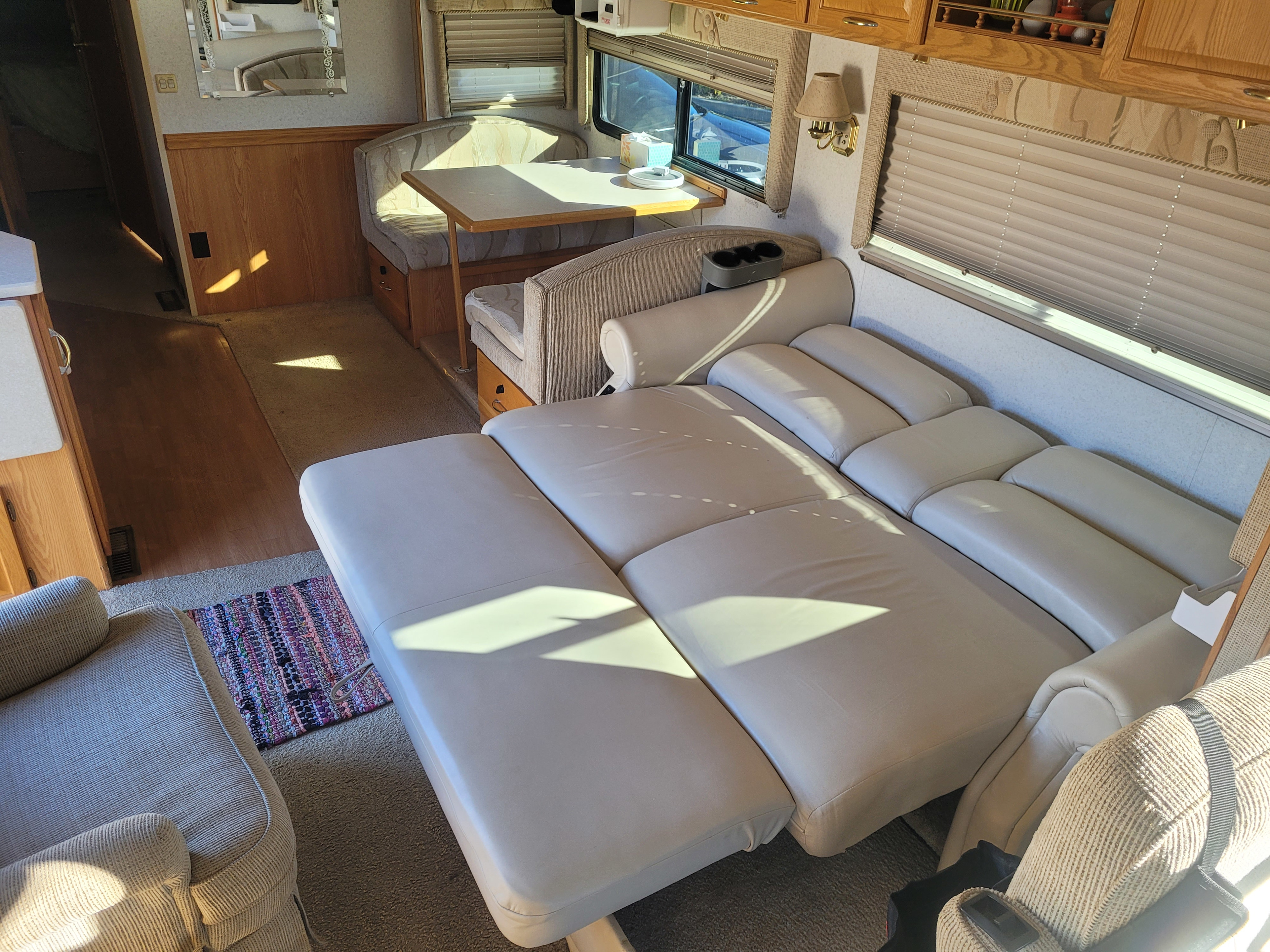 Spacious RV rental interior with a comfortable pull-out sofa bed and a bright dinette area. Ideal for travel.. Itasca Suncruiser 2002