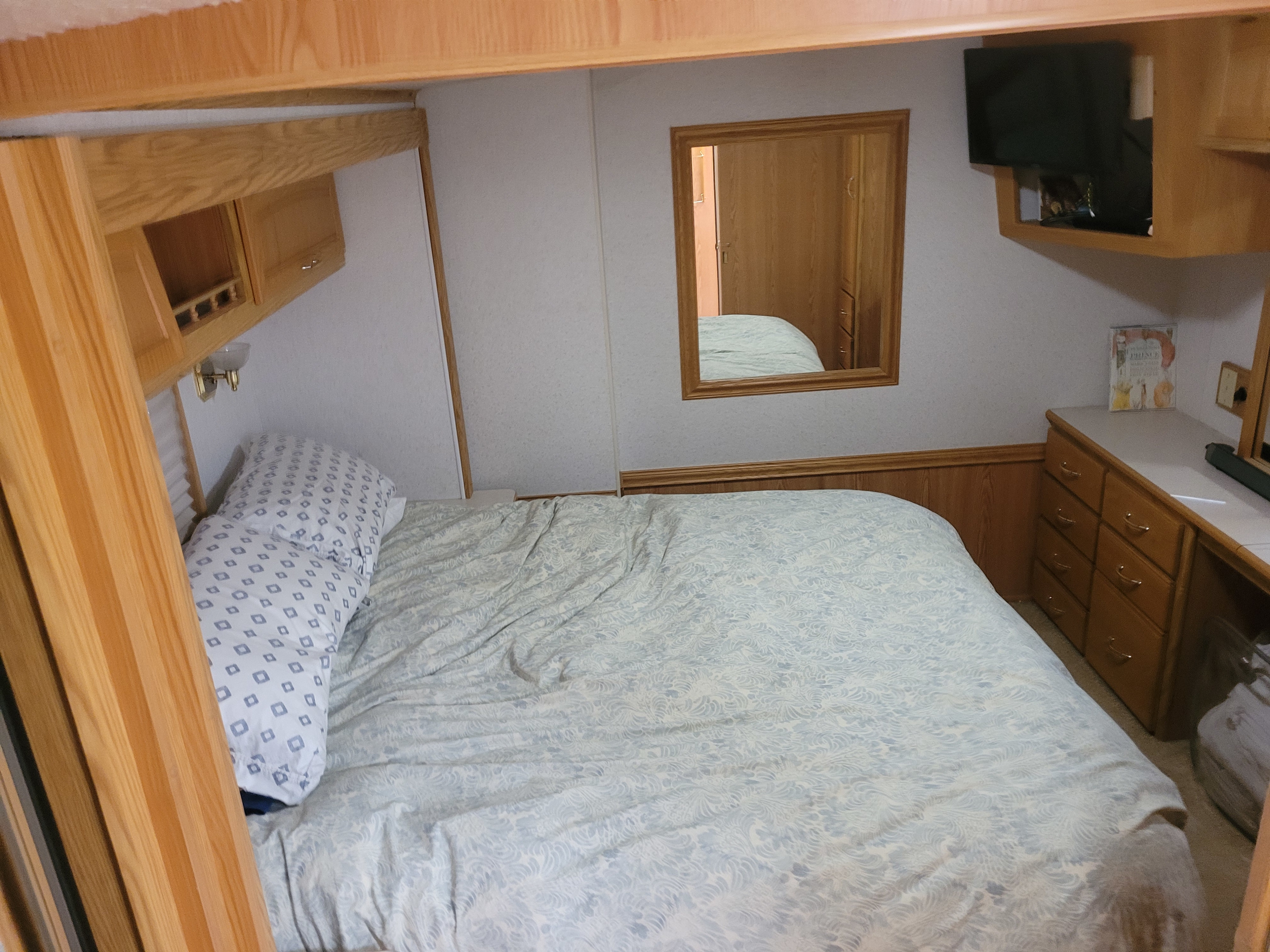 Cozy RV rental bedroom with patterned bed, wooden dresser, mirror, and TV. Ideal for comfortable travel lodging.. Itasca Suncruiser 2002