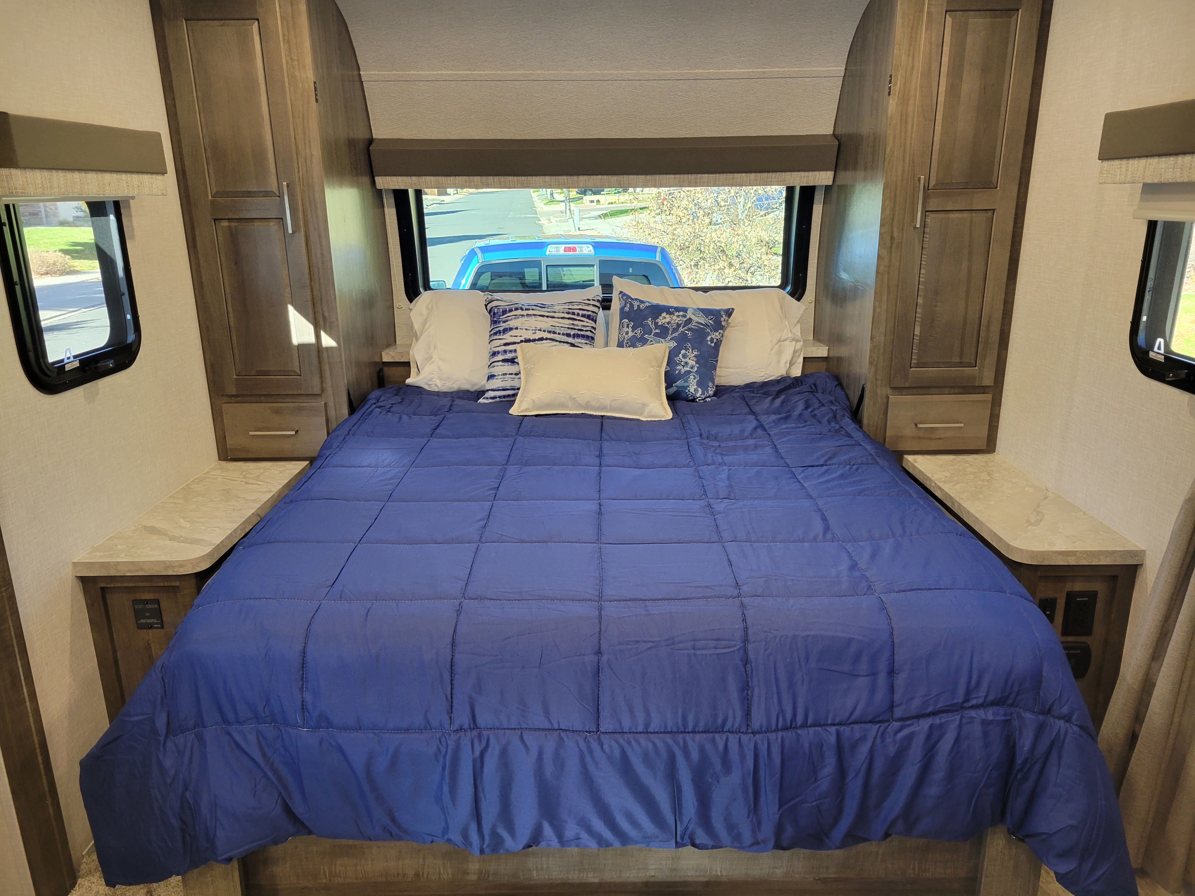 Spacious RV rental bedroom with a comfy blue bed, pillows, side windows, and built-in storage on both sides.. Forest River Flagstaff Micro Lite 2022