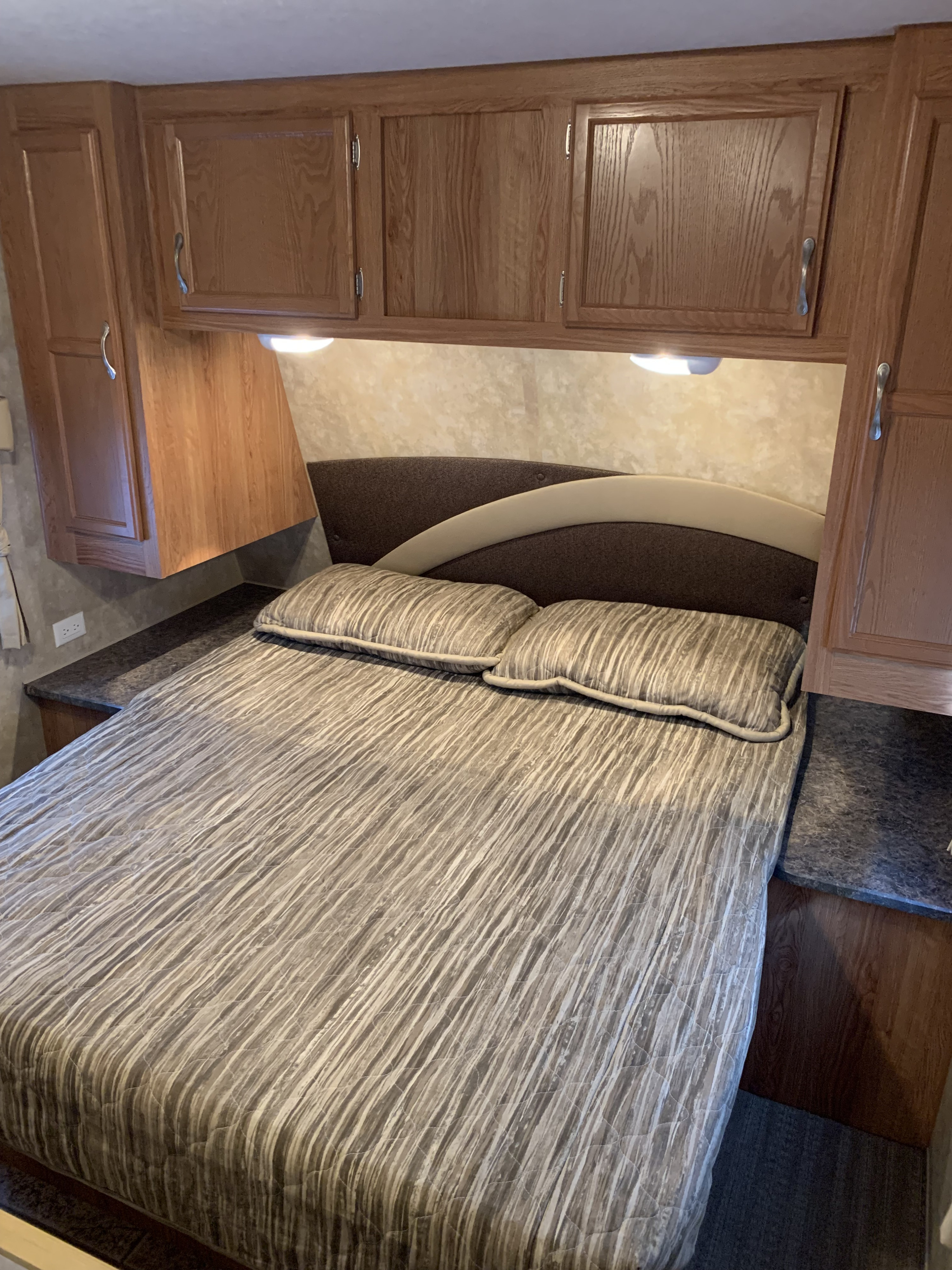 Cozy RV rental bedroom featuring a striped bed, upholstered headboard, and wood cabinetry with accent lights.. Jayco Jay Flight 2010