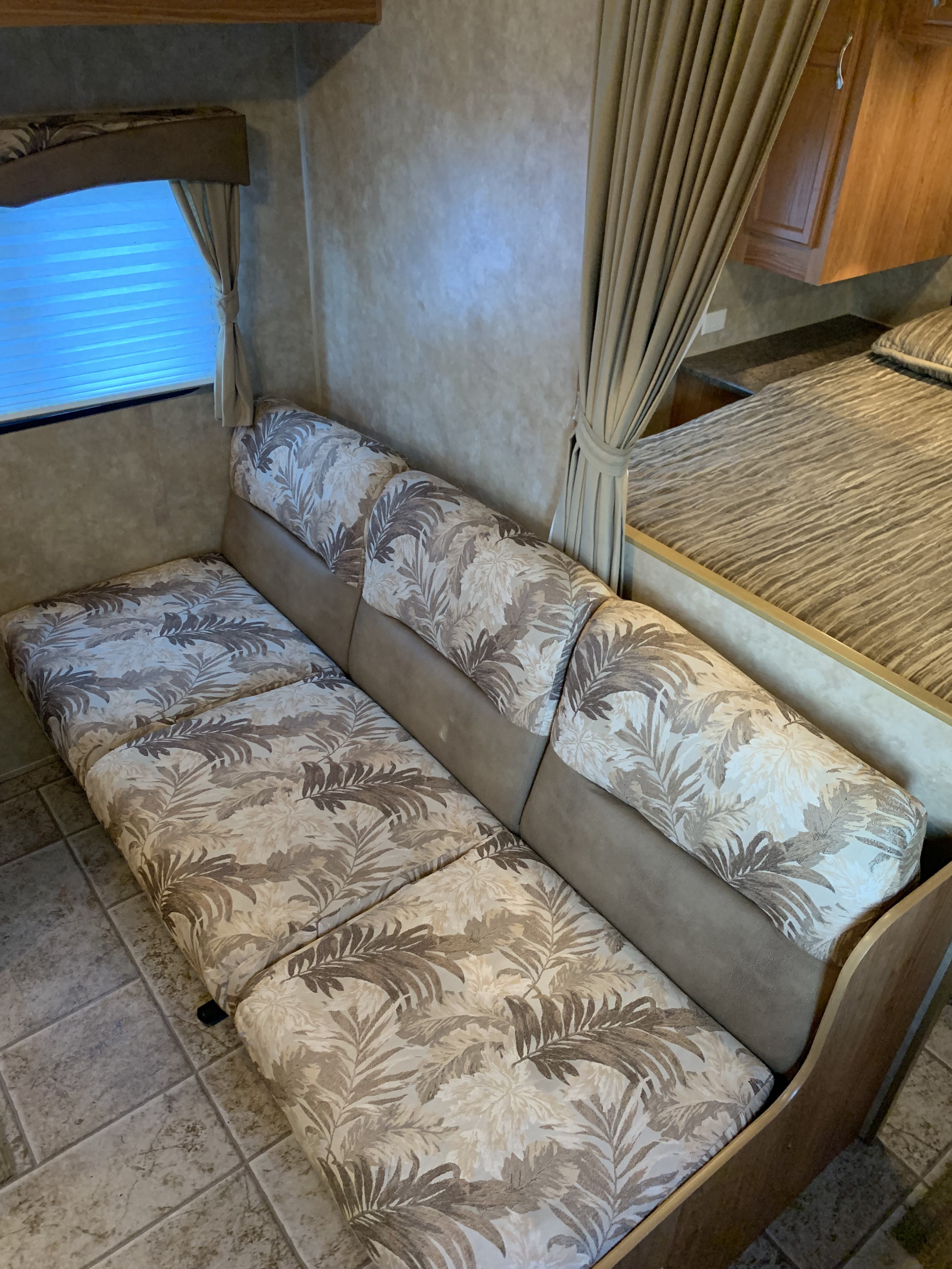 RV rental interior featuring a convertible sofa with leaf pattern cushions, adjacent to a comfortable queen bed and wood cabinetry.. Jayco Jay Flight 2010