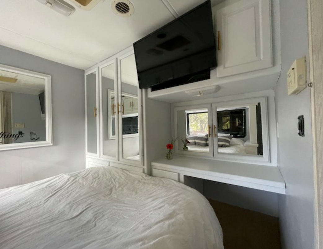 Modern RV rental bedroom features a comfy bed, TV, mirrored cabinets, & vanity with small mirrors.. Other Other 2005