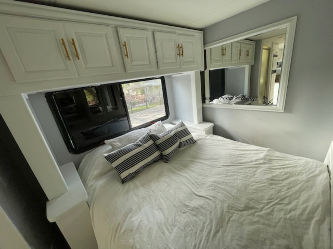 This cozy RV rental bedroom features white overhead cabinets, a comfortable bed, and a large mirror, offering a bright, modern space.. Other Other 2005