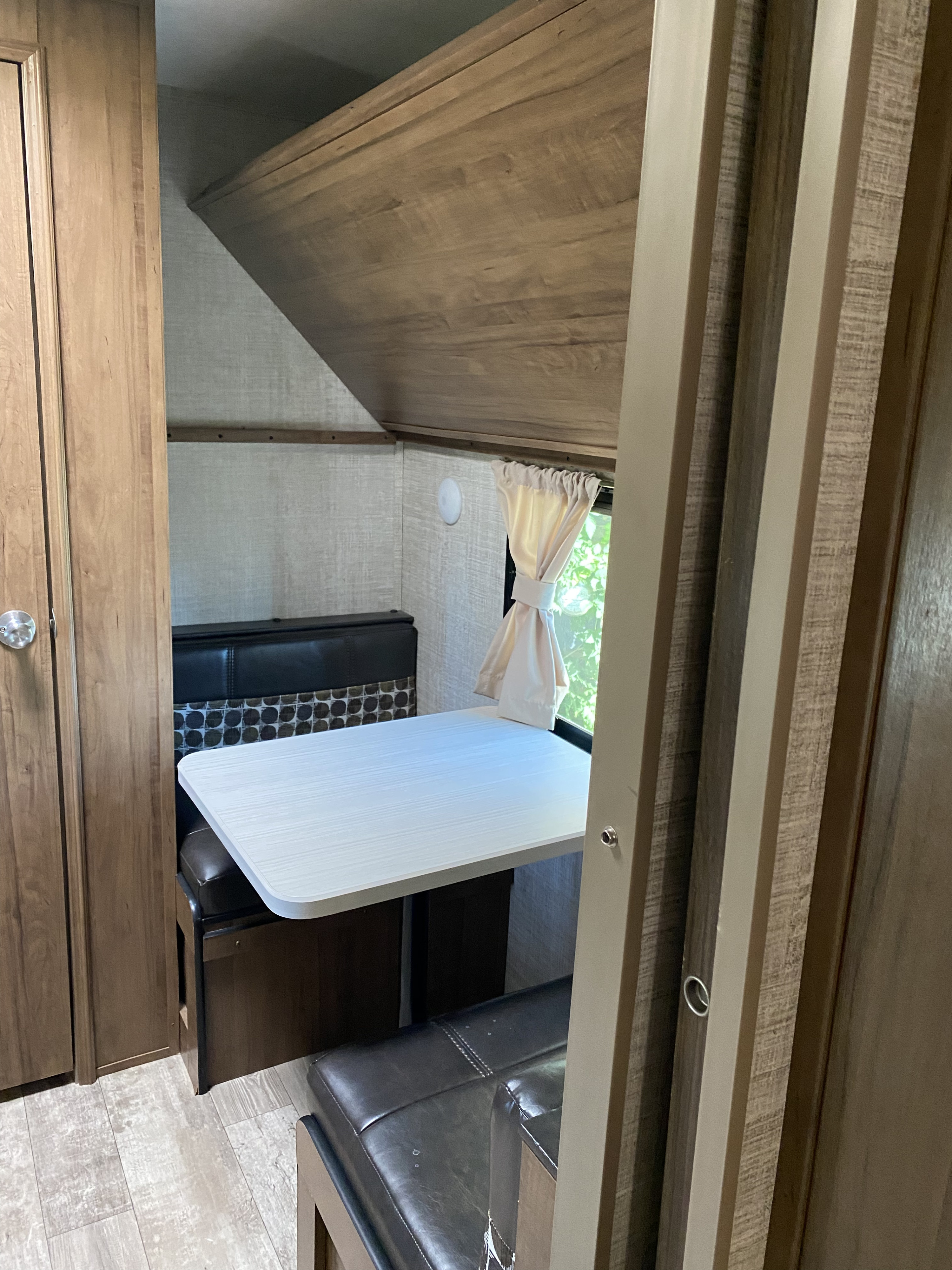 Cozy RV rental interior featuring a dinette with bench seating, a bright window, and an overhead bunk bed.. Gulf Stream Trailmaster 2020