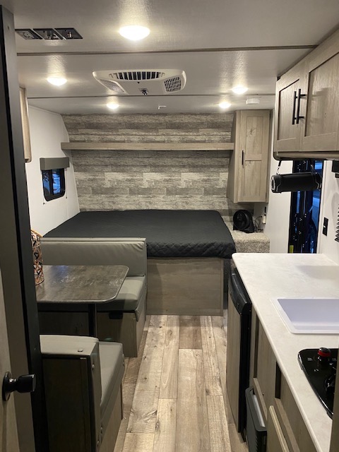 Cozy RV rental interior with a bed, dinette, compact kitchen, and AC unit, featuring wood-look floors.. Other Springdale 2021