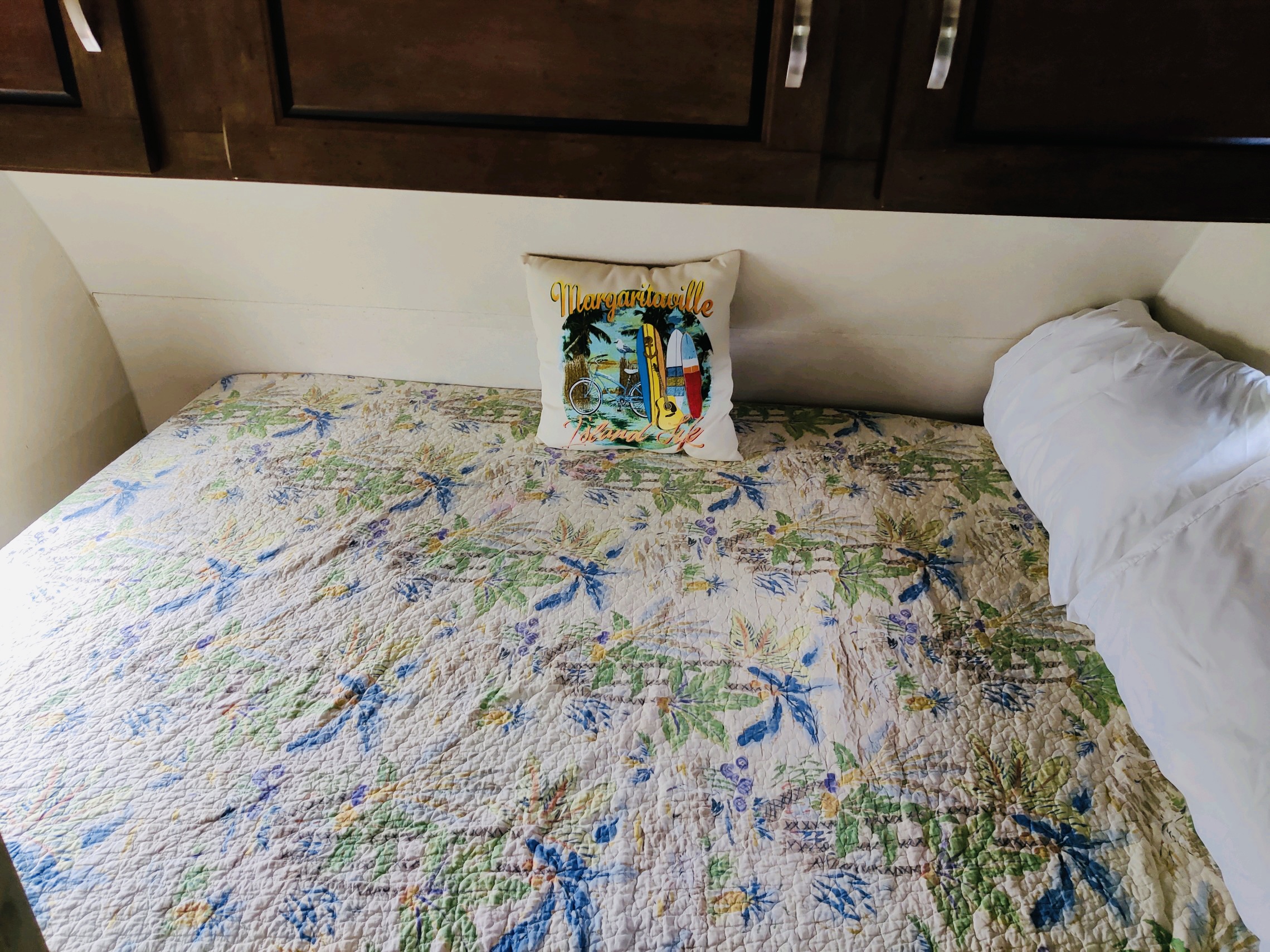 RV rental sleeping area with a tropical quilt, "Margaritaville" pillow, and dark overhead cabinets for a comfortable stay.. Forest River Salem 2018