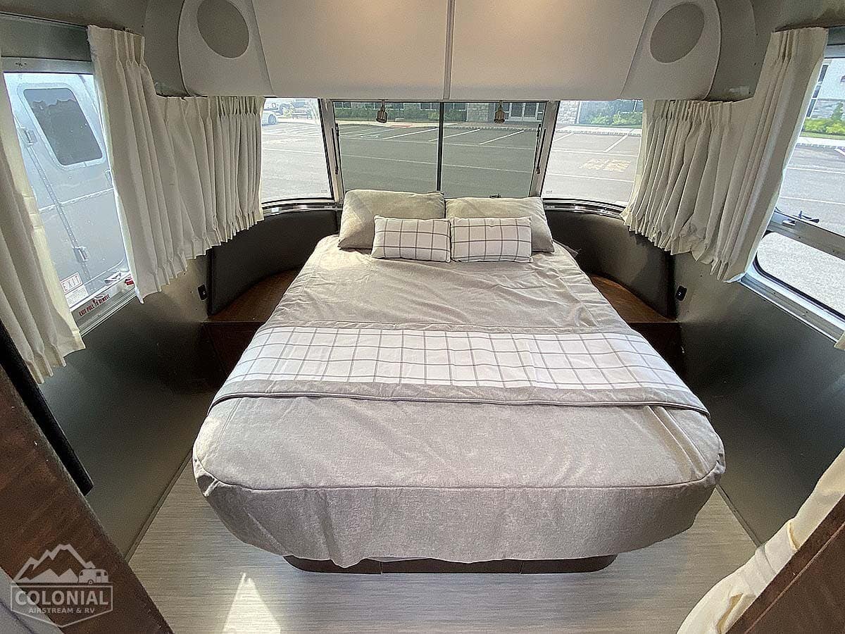 Step into this Airstream rv rental's cozy bedroom. Features a large bed with gray bedding and patterned pillows, ample natural light.. Airstream Globetrotter 2022