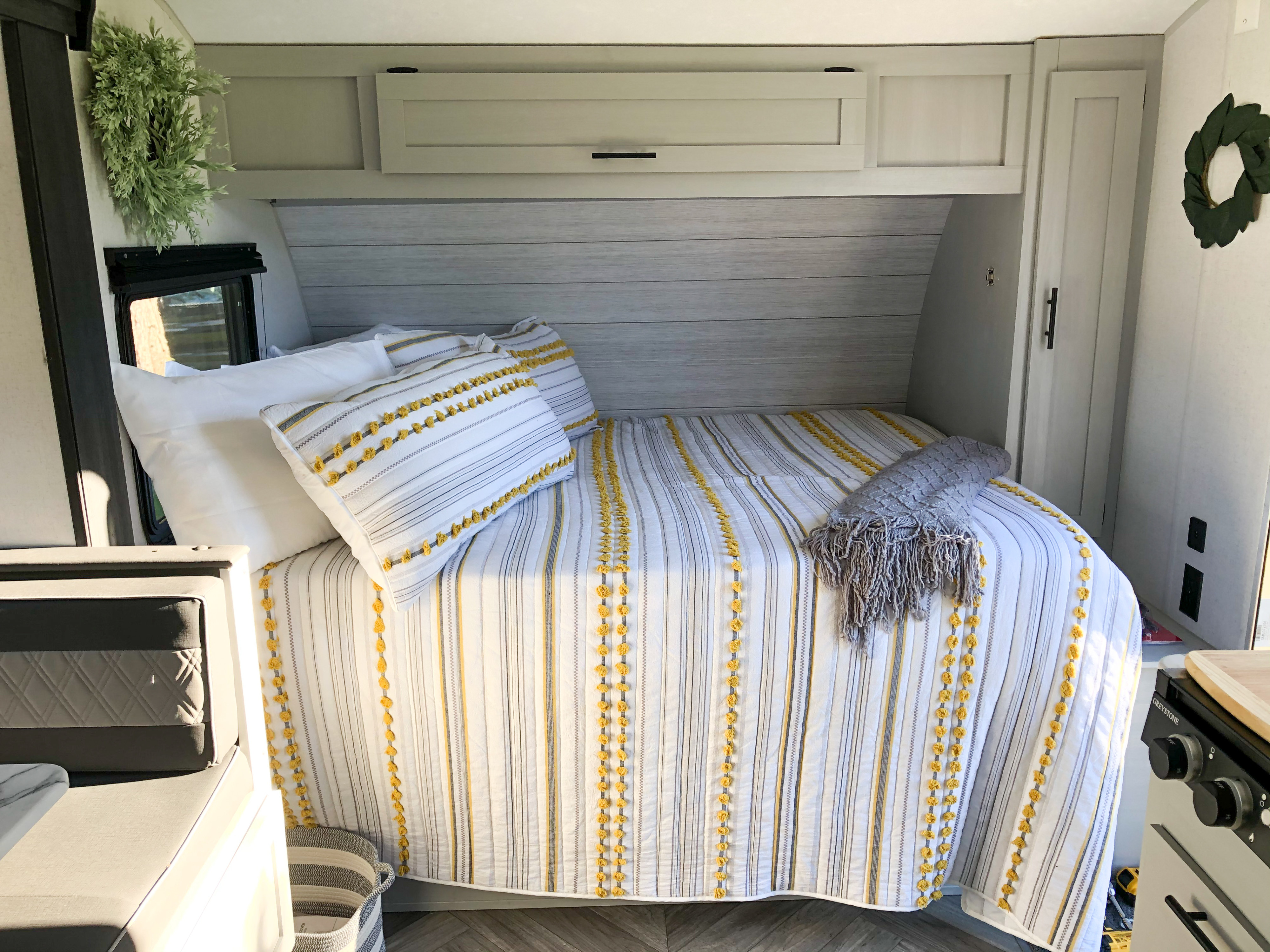 Cozy RV rental bedroom featuring striped yellow and white bedding, practical overhead storage, and natural light from a side window.. Forest River Salem FSX platinum 2021