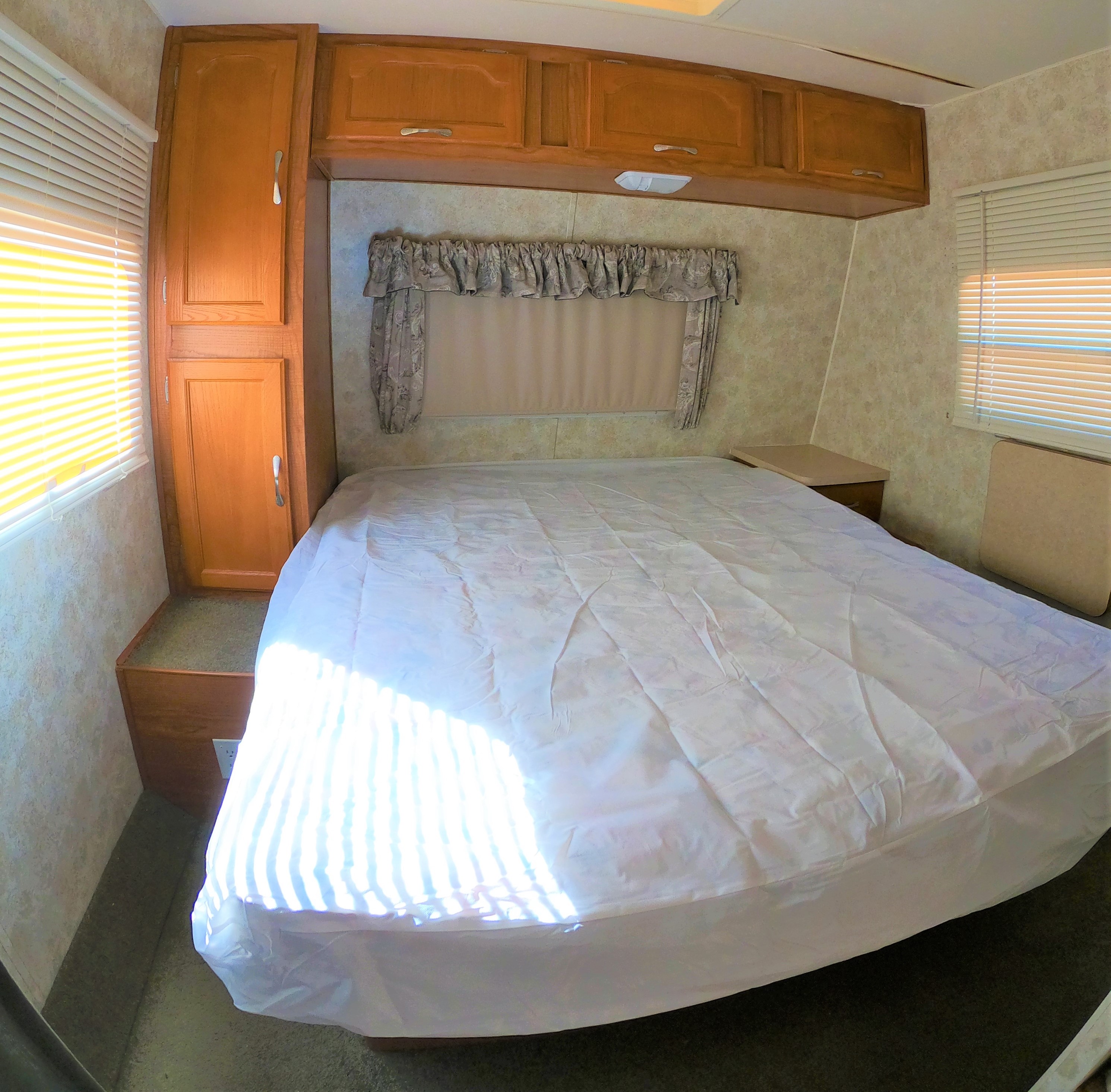 RV rental bedroom with a comfy queen bed, ample wooden storage cabinets, bright window blinds, and carpeted floor.. Coachmen Other 2005