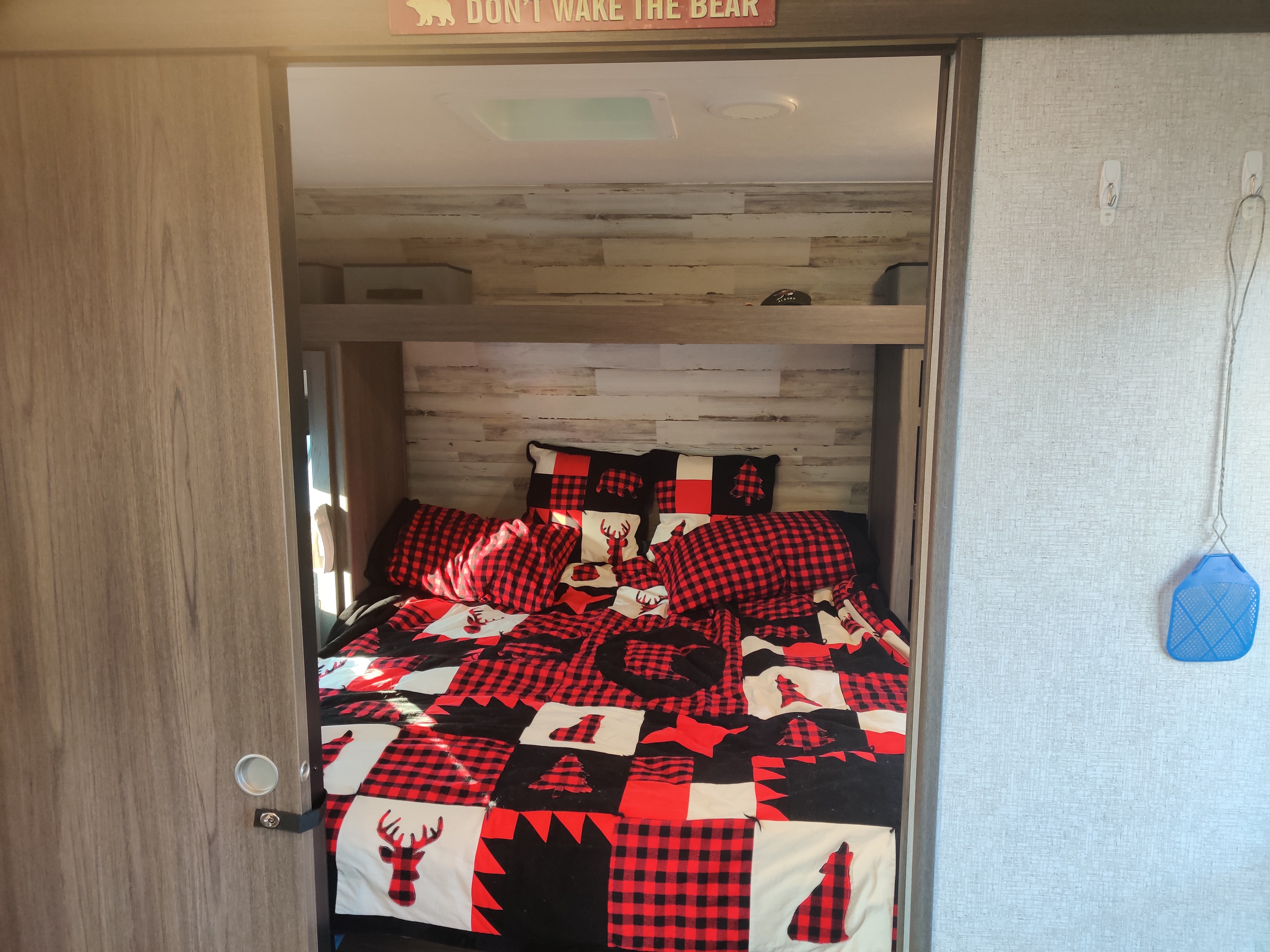 RV rental bedroom: cozy with red and black plaid bedding featuring wildlife, a bear sign, and rustic wood-look walls.. Dutchmen Kodiak 2021