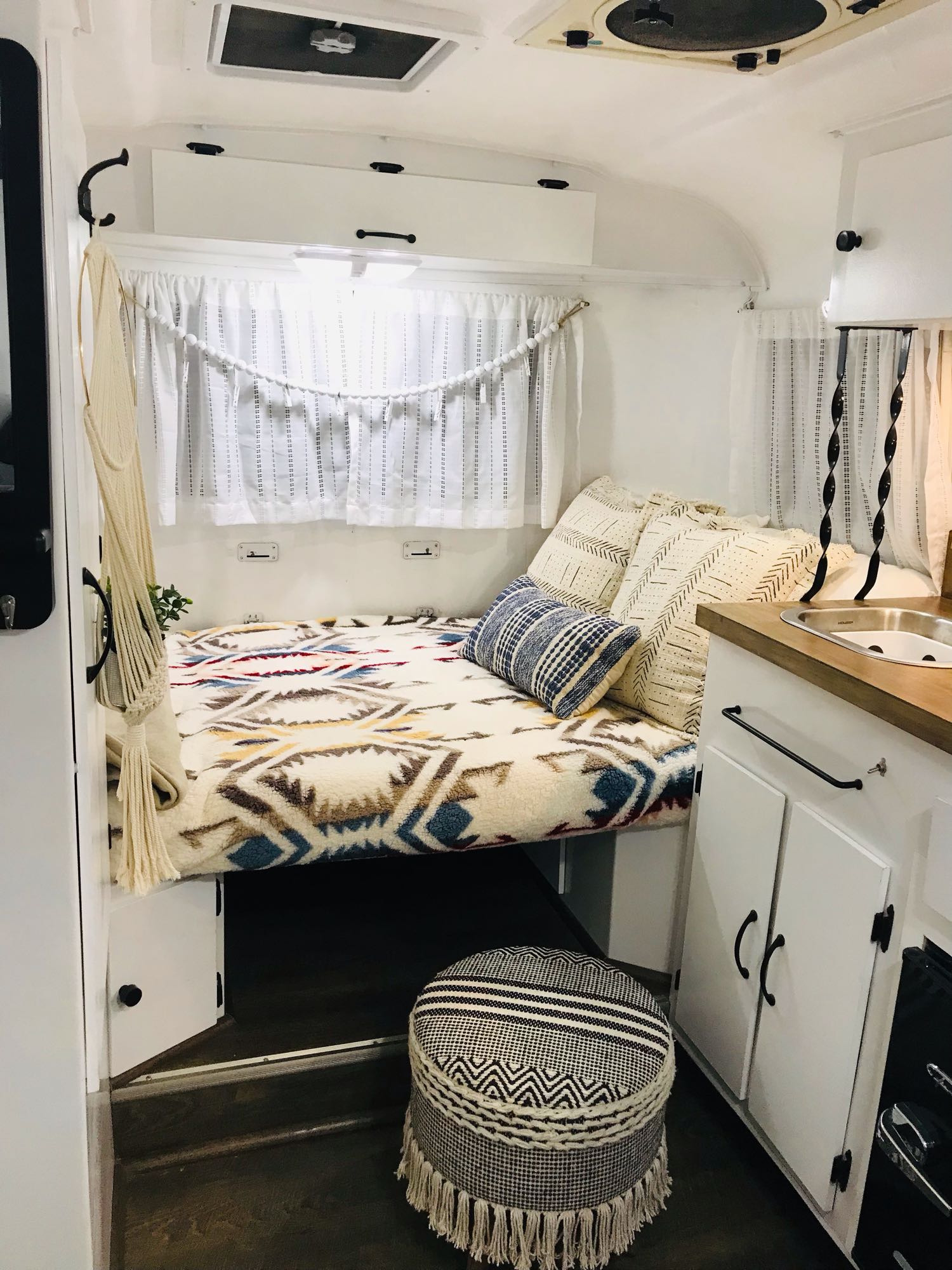 Inviting RV rental interior showcasing a cozy bed with patterned blankets/pillows, compact kitchen, and white decor.. Scamp 13' 1979