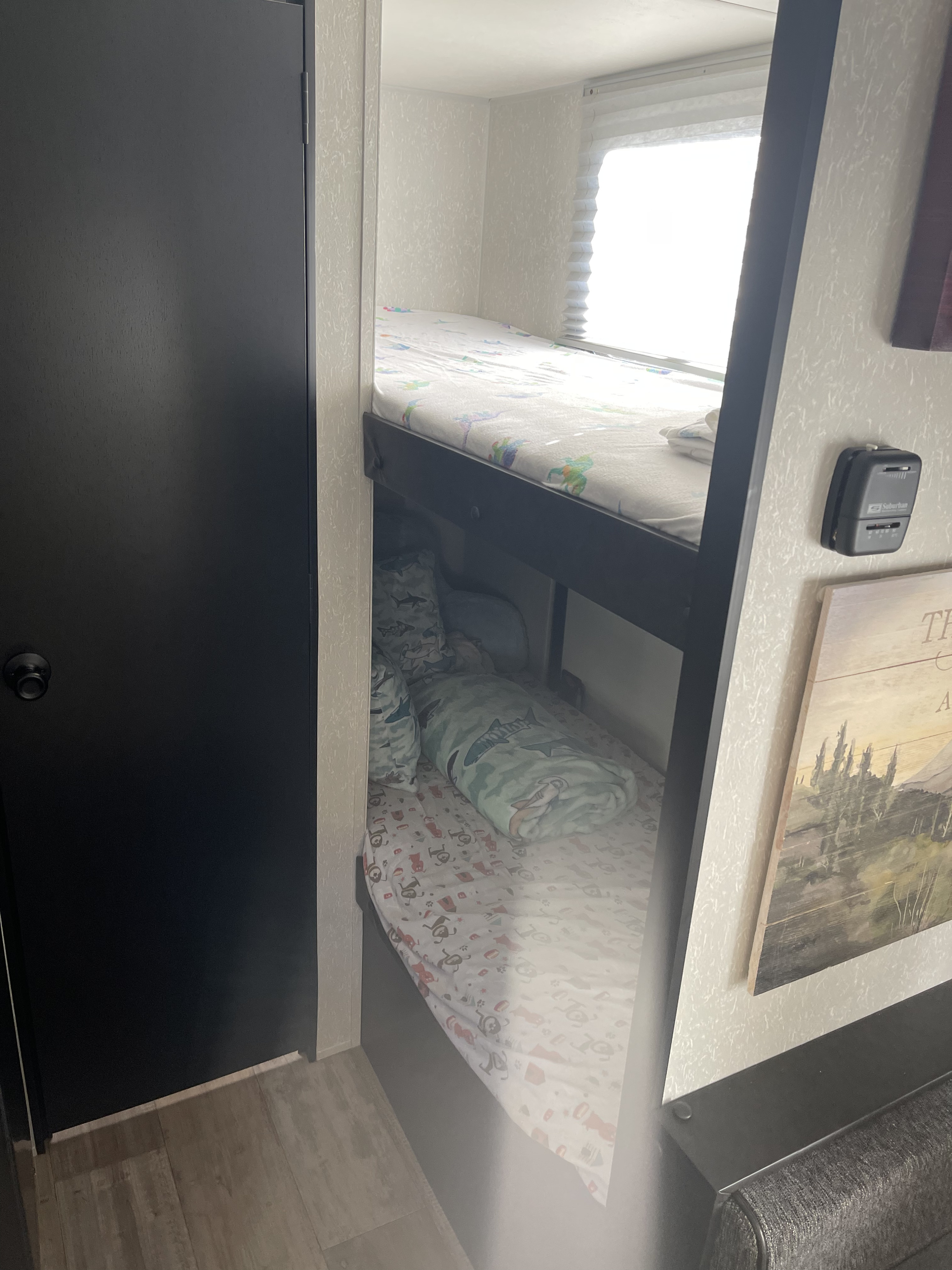 Inside an RV rental: two bunk beds with patterned sheets, a window, and a door, showing compact, cozy sleeping quarters.. Forest River Cherokee Wolf Pup 2022