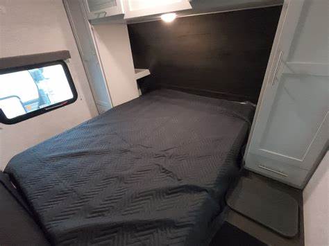 Cozy RV rental bedroom featuring a dark grey bed, window, and built-in cabinets for a comfortable sleeping area.. Keystone Bullet 2020