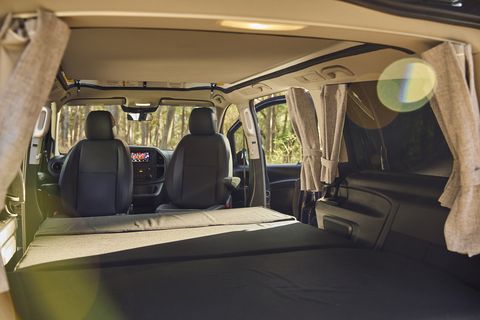 RV rental interior from rear: a comfy bed fills the back, with front seats and curtains visible. Ready for camping trips.. Mercedes-Benz Metris 2021