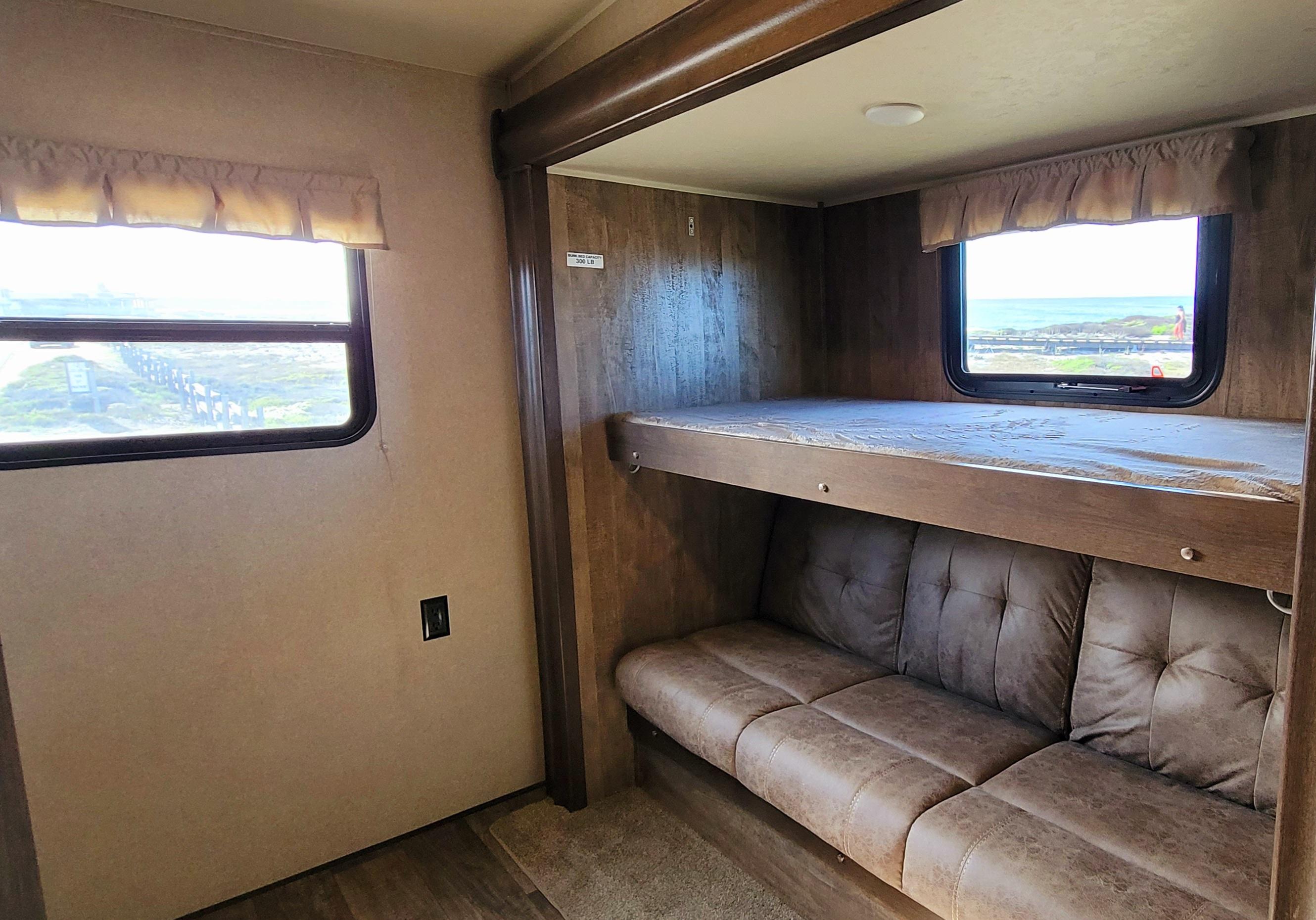 RV rental bunk bed area with a sofa below, offering a beautiful beach and ocean view from its windows.. Forest River Puma 2018