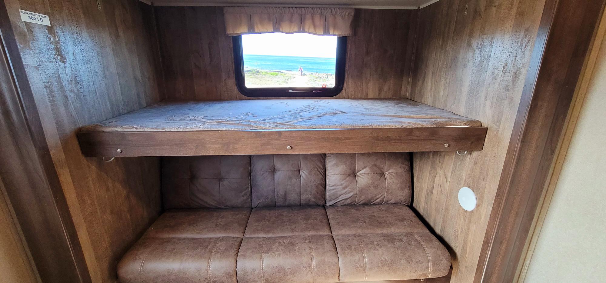 Cozy RV rental bunk setup with an ocean view. Features a 300 lb capacity top bunk and a sofa bed below.. Forest River Puma 2018