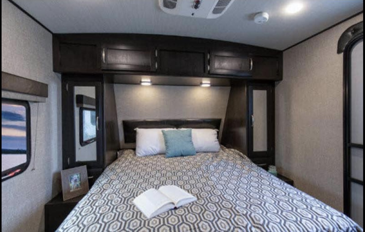 Cozy RV rental bedroom with a comfortable bed, overhead storage, and a window to enjoy the scenic views on your trip.. Grand Design Imagine 2019