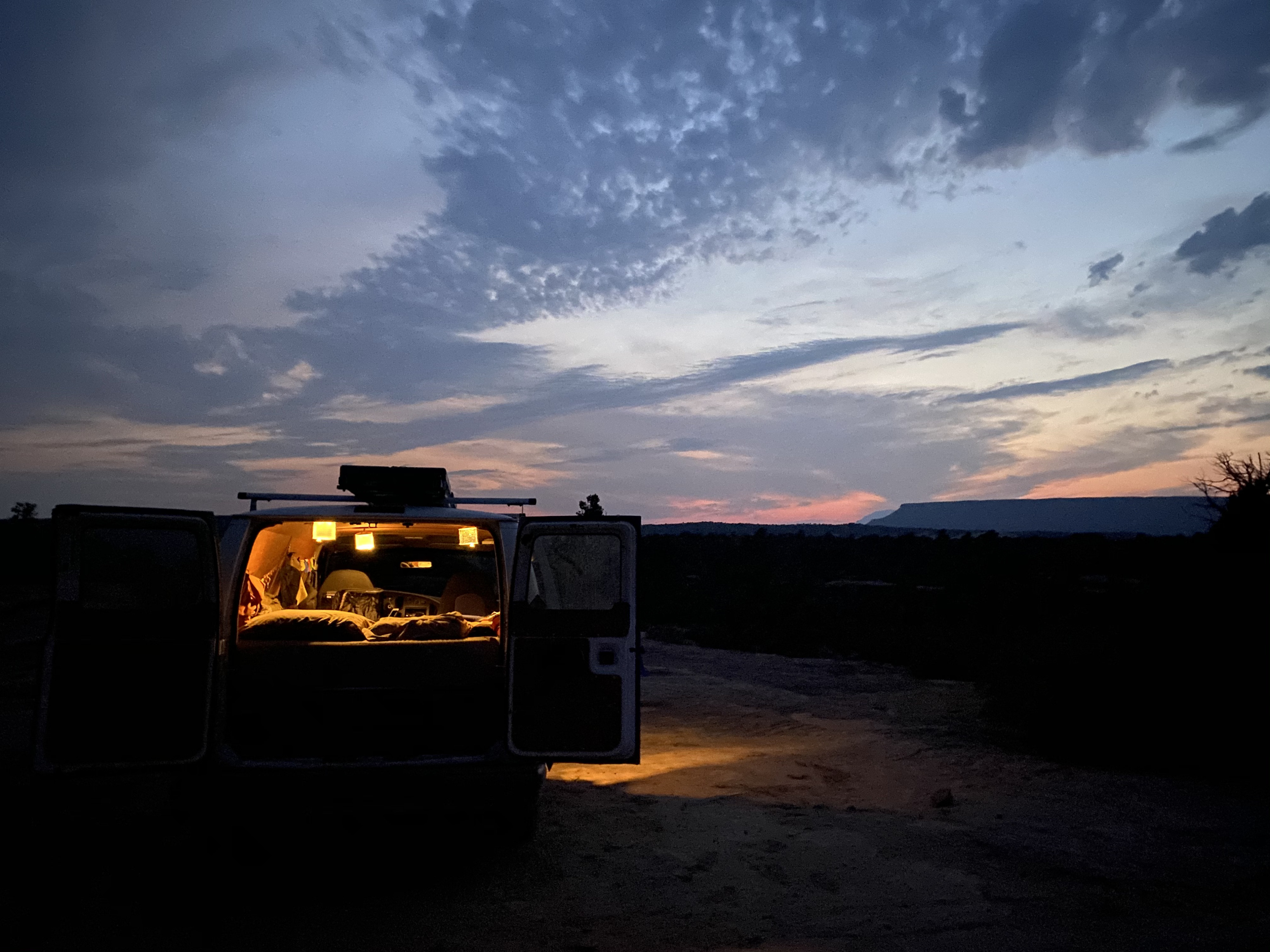RV rental parked at dusk with illuminated interior and open doors, offering a view of a flat-topped mountain under a colorful sky.. Ford Econolline 250s 2001