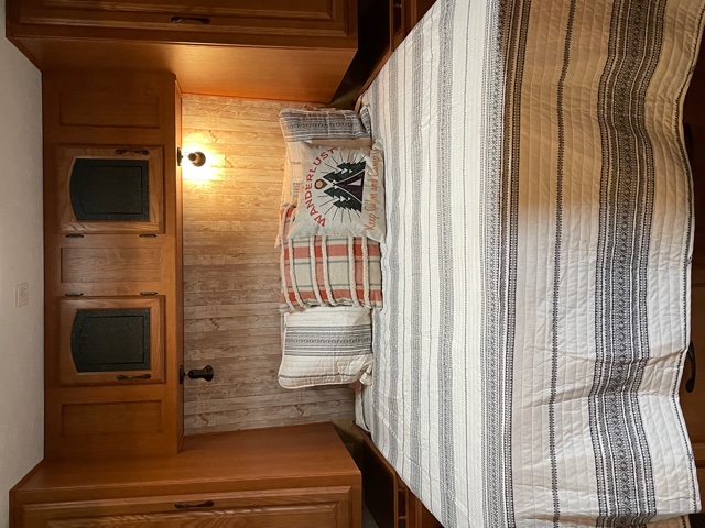 Cozy RV rental bedroom with striped quilt, wanderlust pillow, wood paneling, and built-in cabinets.. Forest River Sandpiper 2011