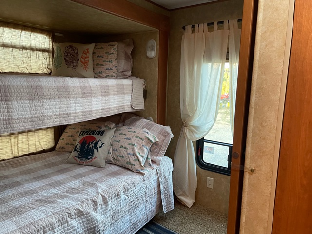 Comfortable bunk beds inside an RV rental, featuring themed pillows and window views for your next adventure.. Forest River Sandpiper 2011