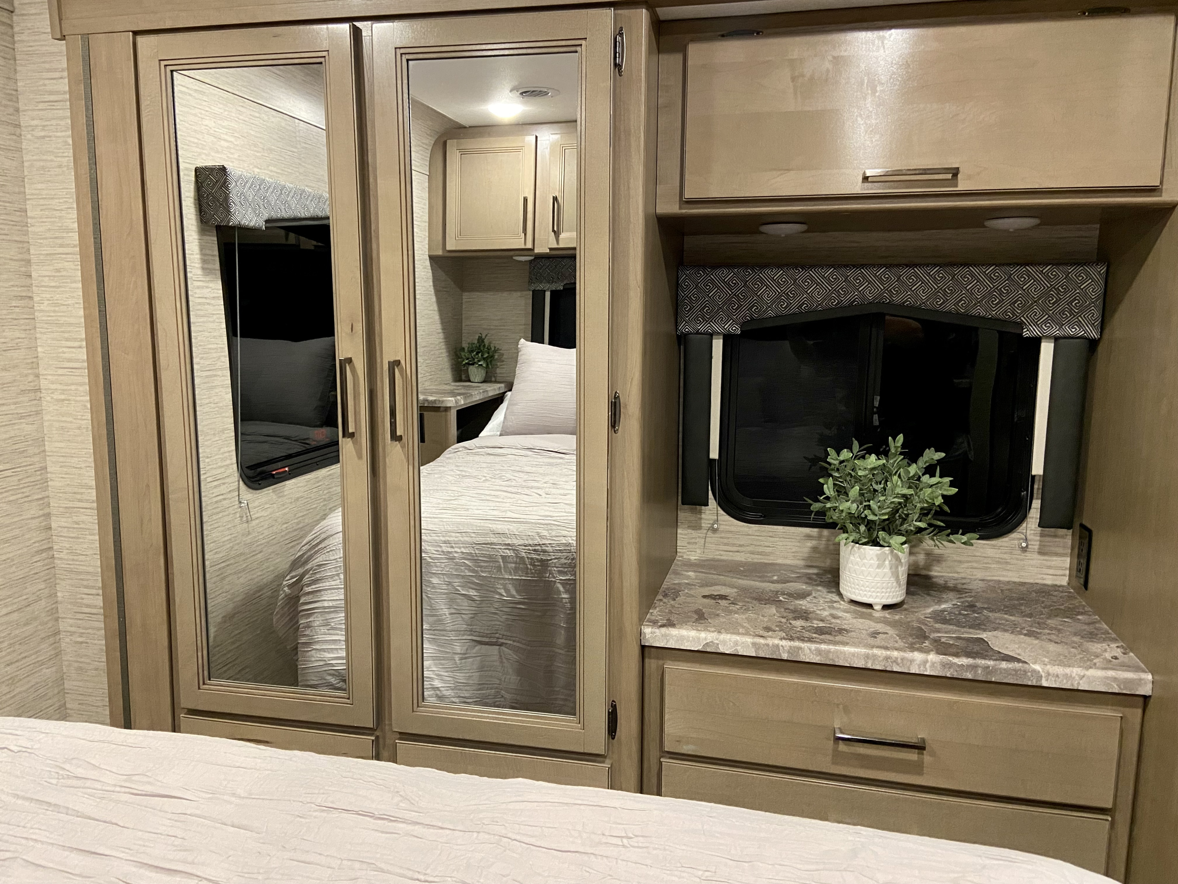 Inside an RV rental: a bright bedroom with mirrored closets, comfortable bed, and wood storage cabinets.. Other Other 2022