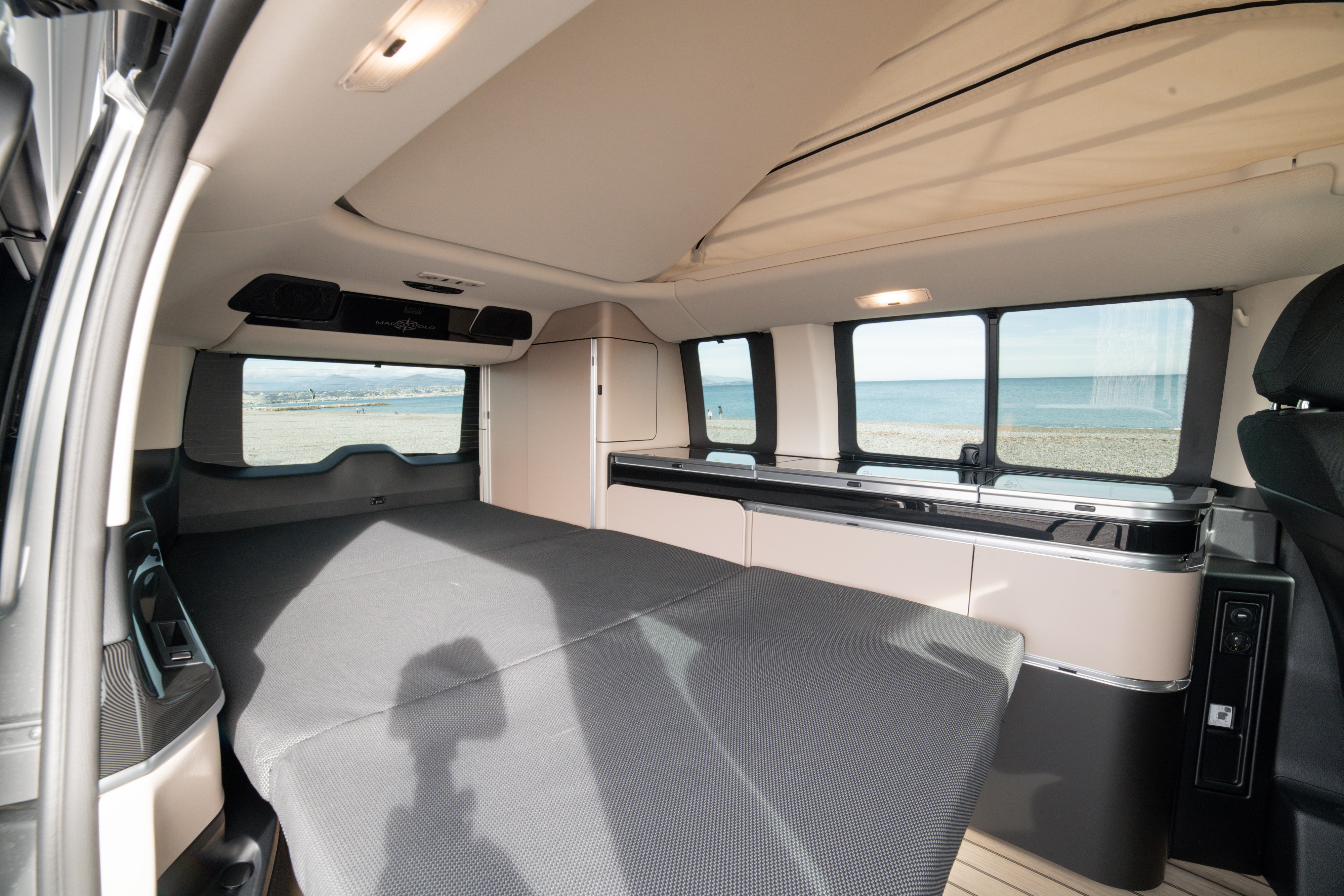 Interior of a comfortable Mercedes-Benz Marco Polo camper van for RV rental, with a bed, kitchen, and scenic beach view.. Mercedes Marco Polo 2022