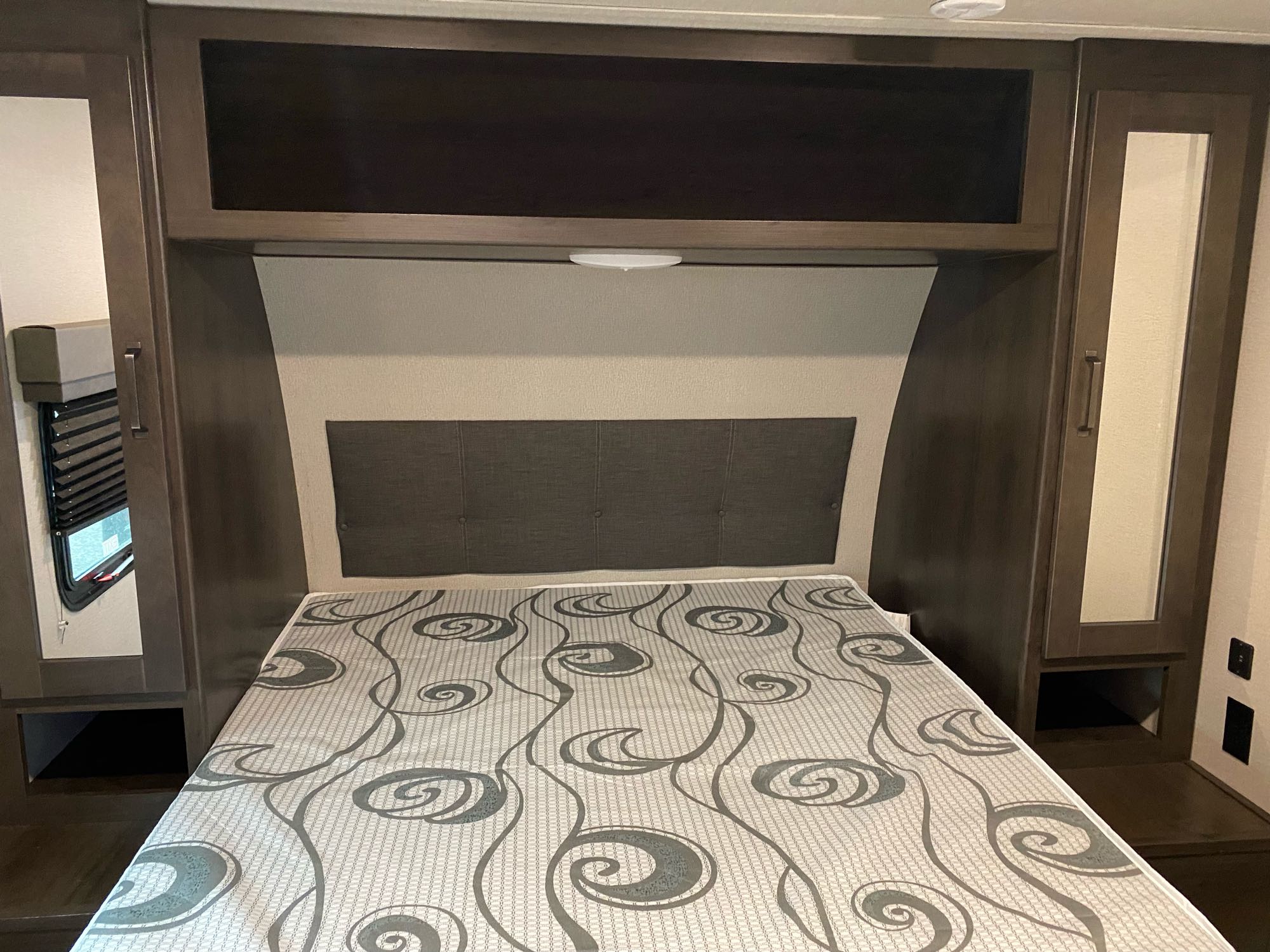 Inside an RV rental: a compact bedroom with bed, headboard, overhead cabinets, and mirrored wardrobes.. Grand Design Transcend 2022