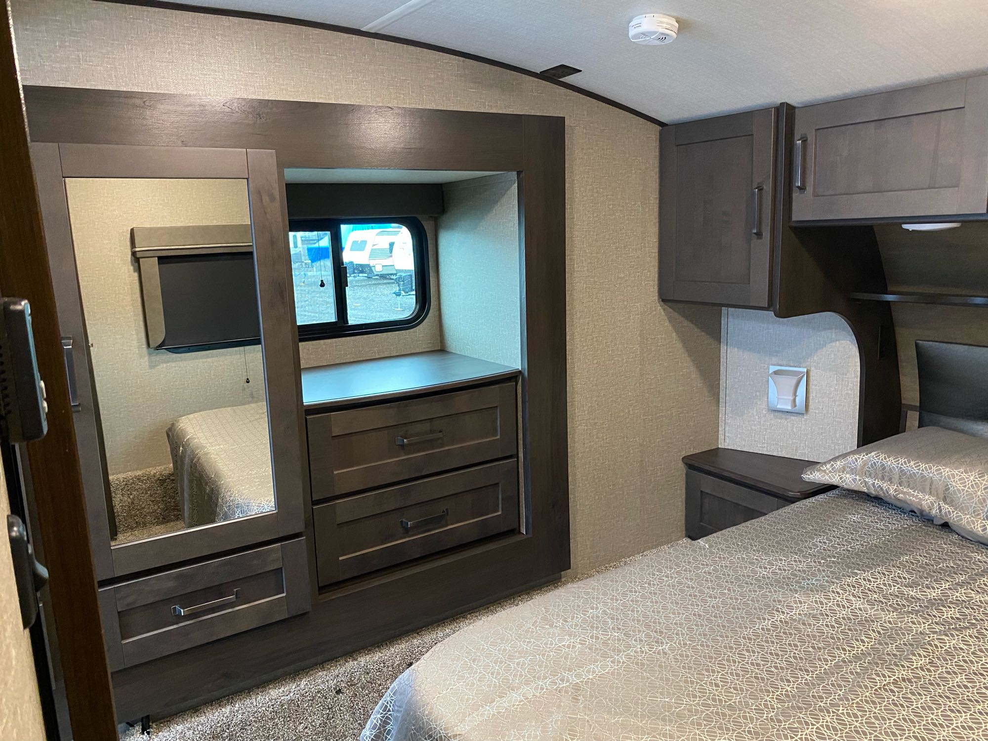 RV rental bedroom featuring a patterned bed, nightstand, overhead cabinets, and a mirrored closet with integrated drawers.. Grand Design Reflection 2022