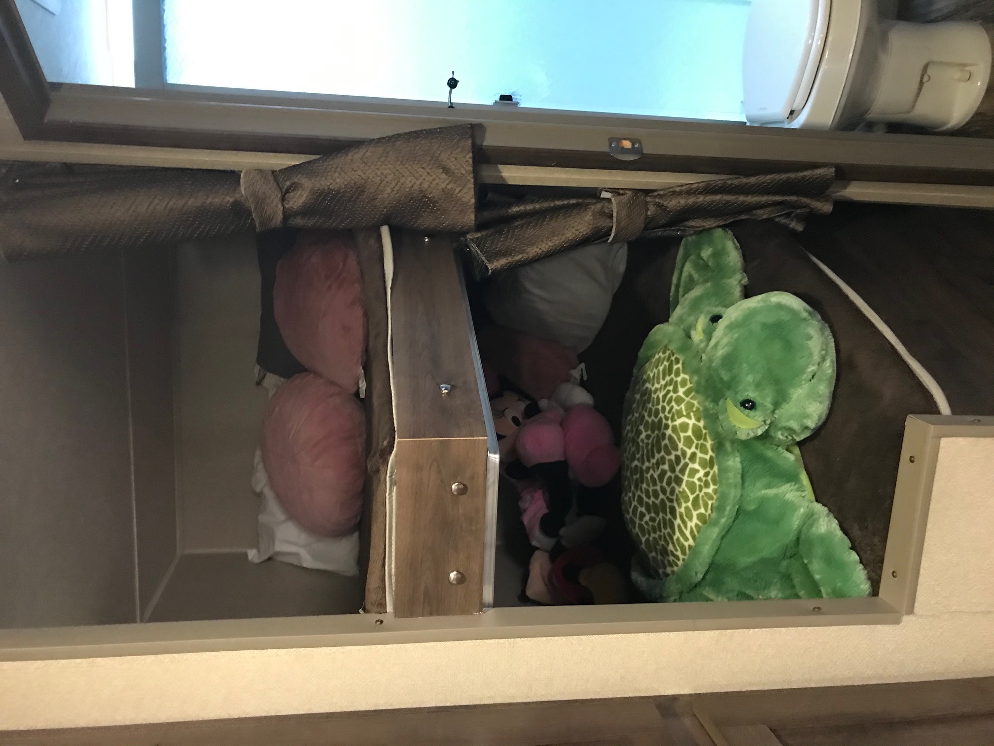 Organized RV rental overhead storage: pillows & plush toys. Compact camper space with window and partial toilet view.. Palomino Puma 2016