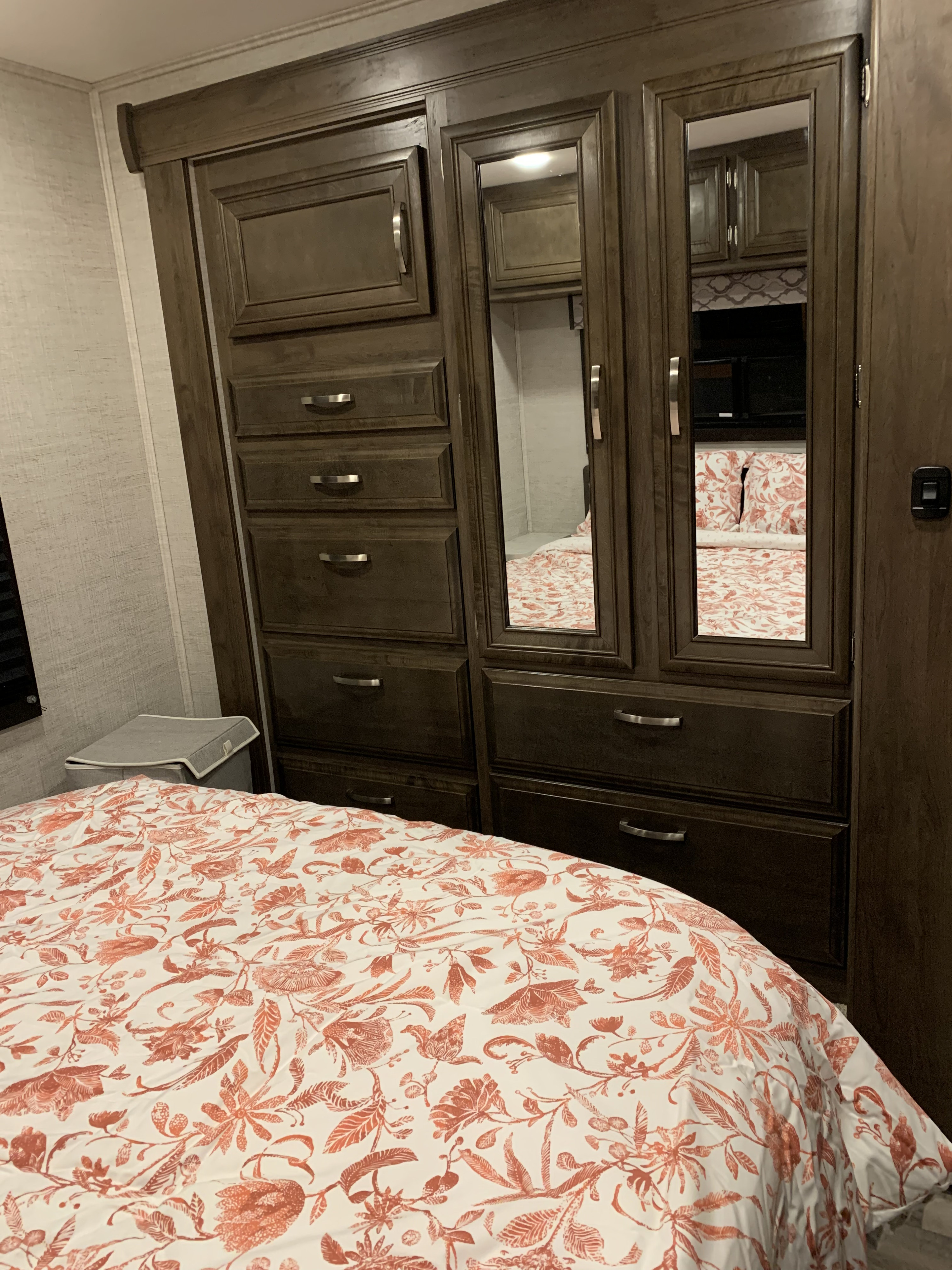 Interior of an RV rental bedroom showing a dark wood wardrobe with mirrored doors reflecting the floral bedding and compact storage.. Ford Jayco RedHawk 2021