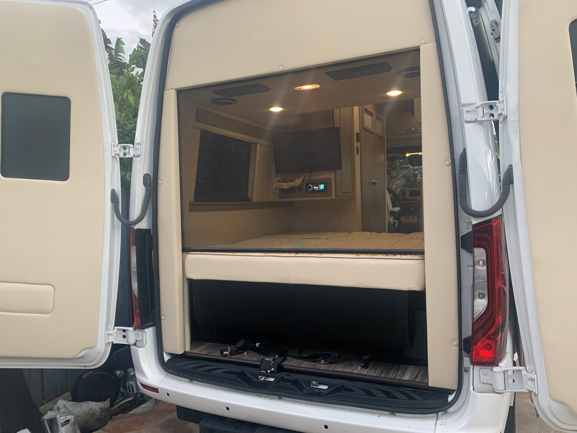 RV rental: View of a modern camper van's custom interior with bed, TV, and lights, seen from the open rear doors.. Midwest Automotive Designs Midwest Automotive Designs Class B 2021