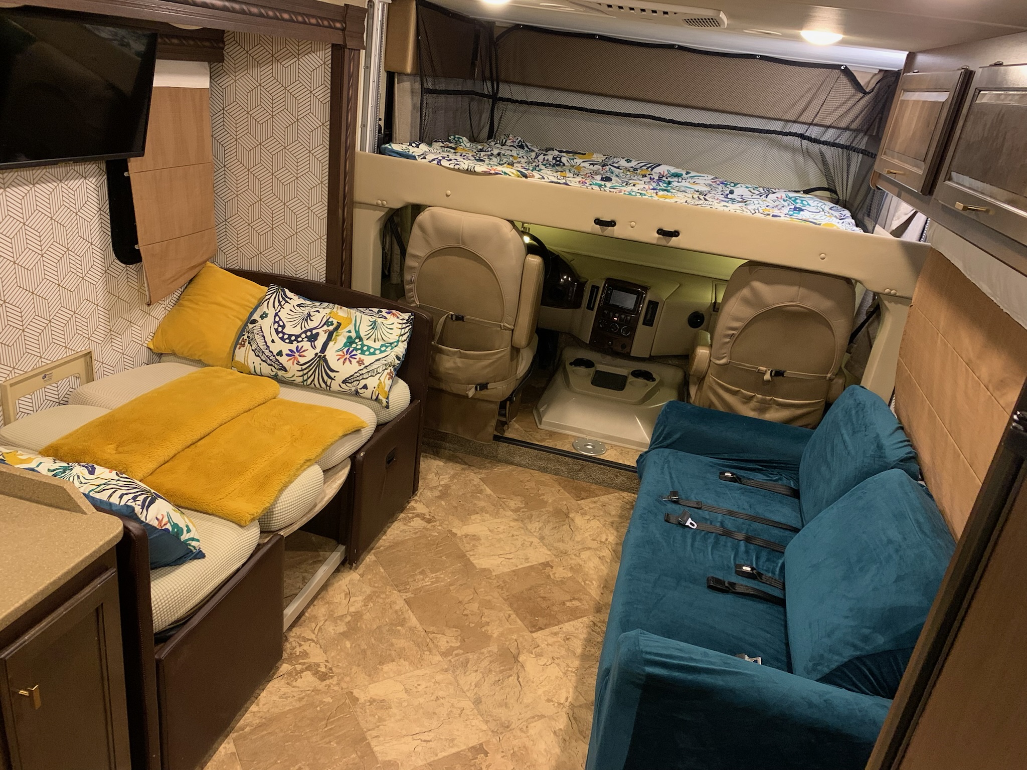 Spacious rv rental interior: bunk bed over cockpit, dinette with yellow pillows, and a teal sofa.. Thor Motor Coach Windsport 2018