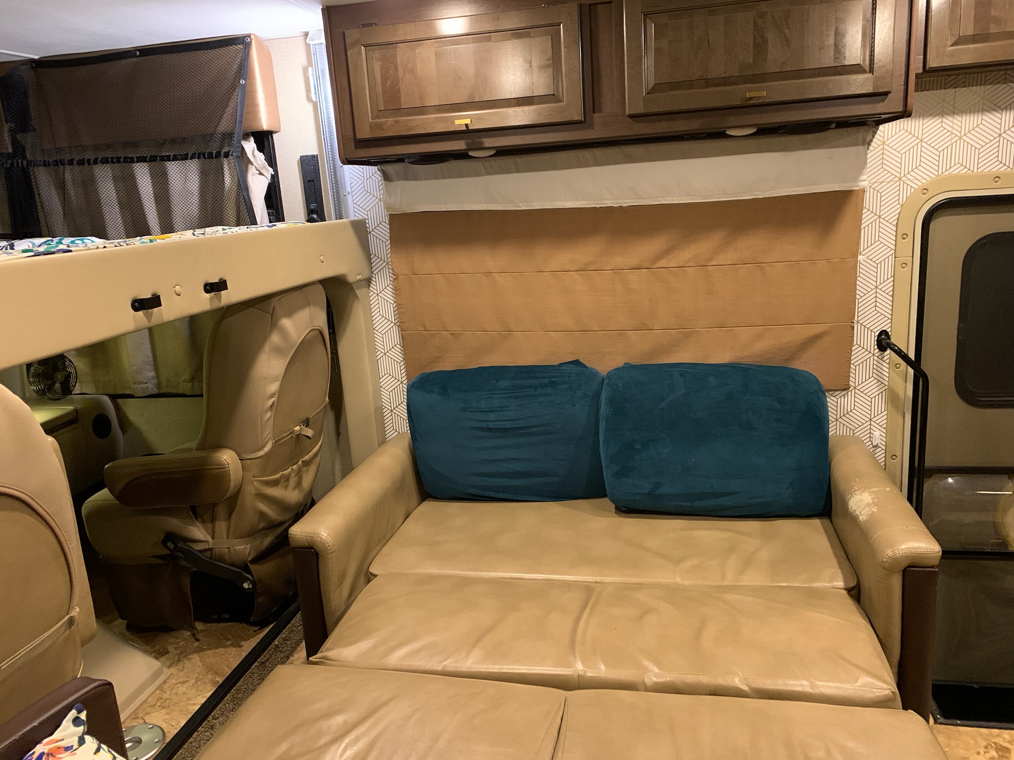 RV rental interior shows a beige pull-out sofa bed with teal pillows, overhead cabinets, and a mesh-netted bunk bed.. Thor Motor Coach Windsport 2018