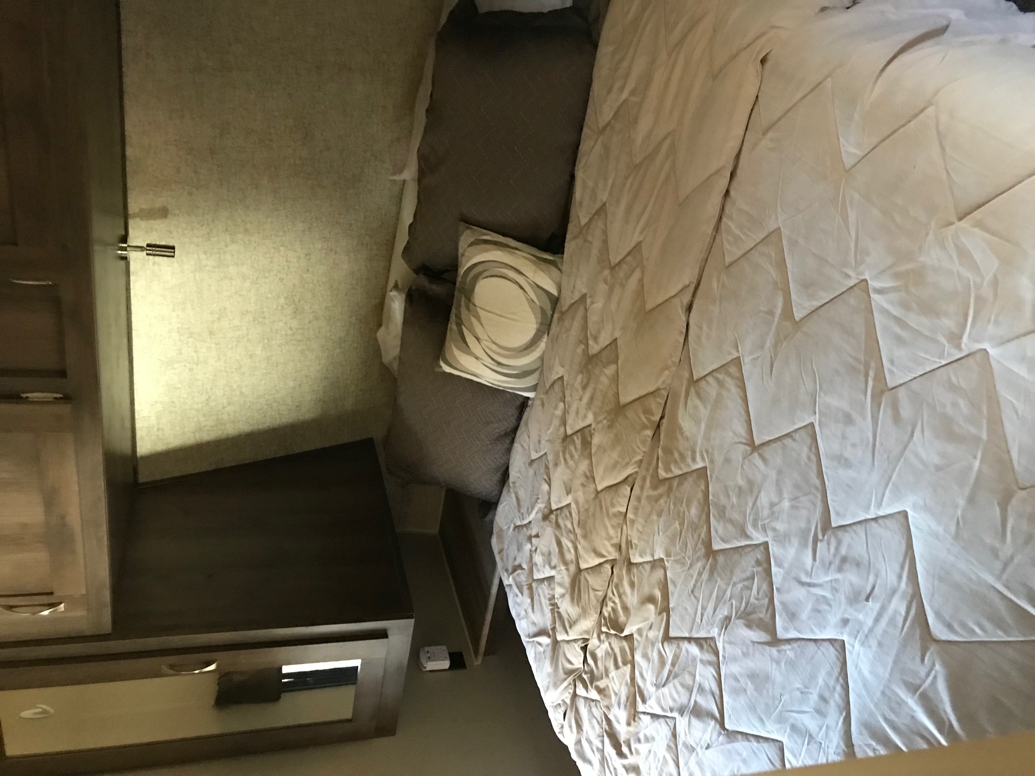 Inside an RV rental: a cozy bedroom with a light-colored, geometric patterned comforter, pillows, and functional wood cabinetry.. Palomino Puma 2016